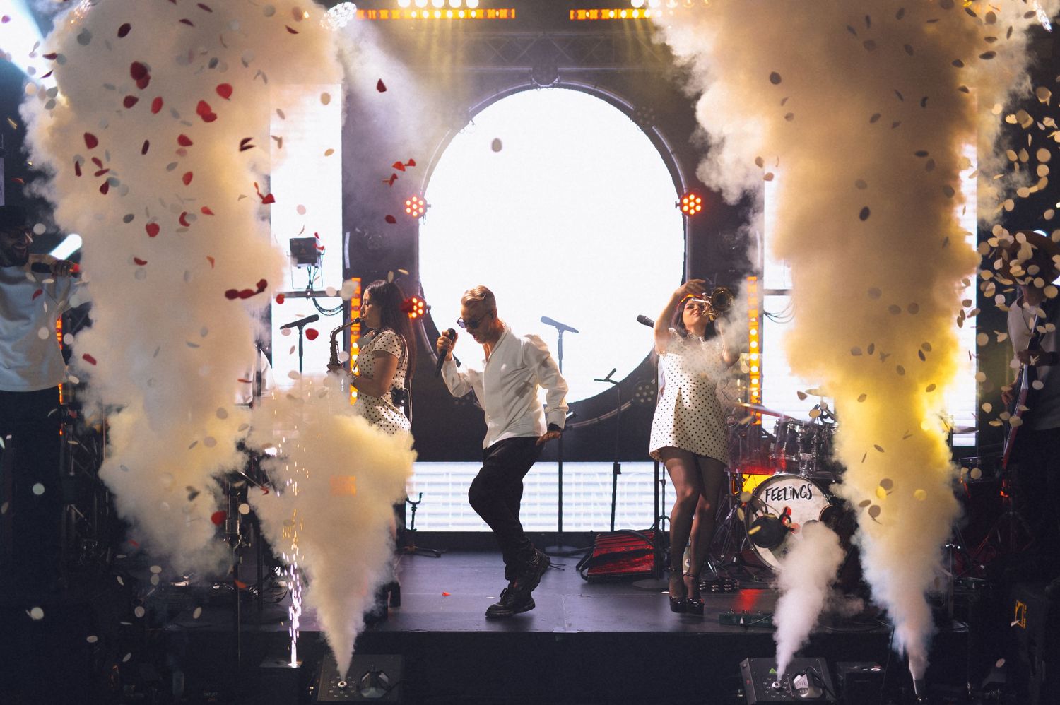 Two performers dance on stage amid white smoke and colorful confetti during a live concert event.