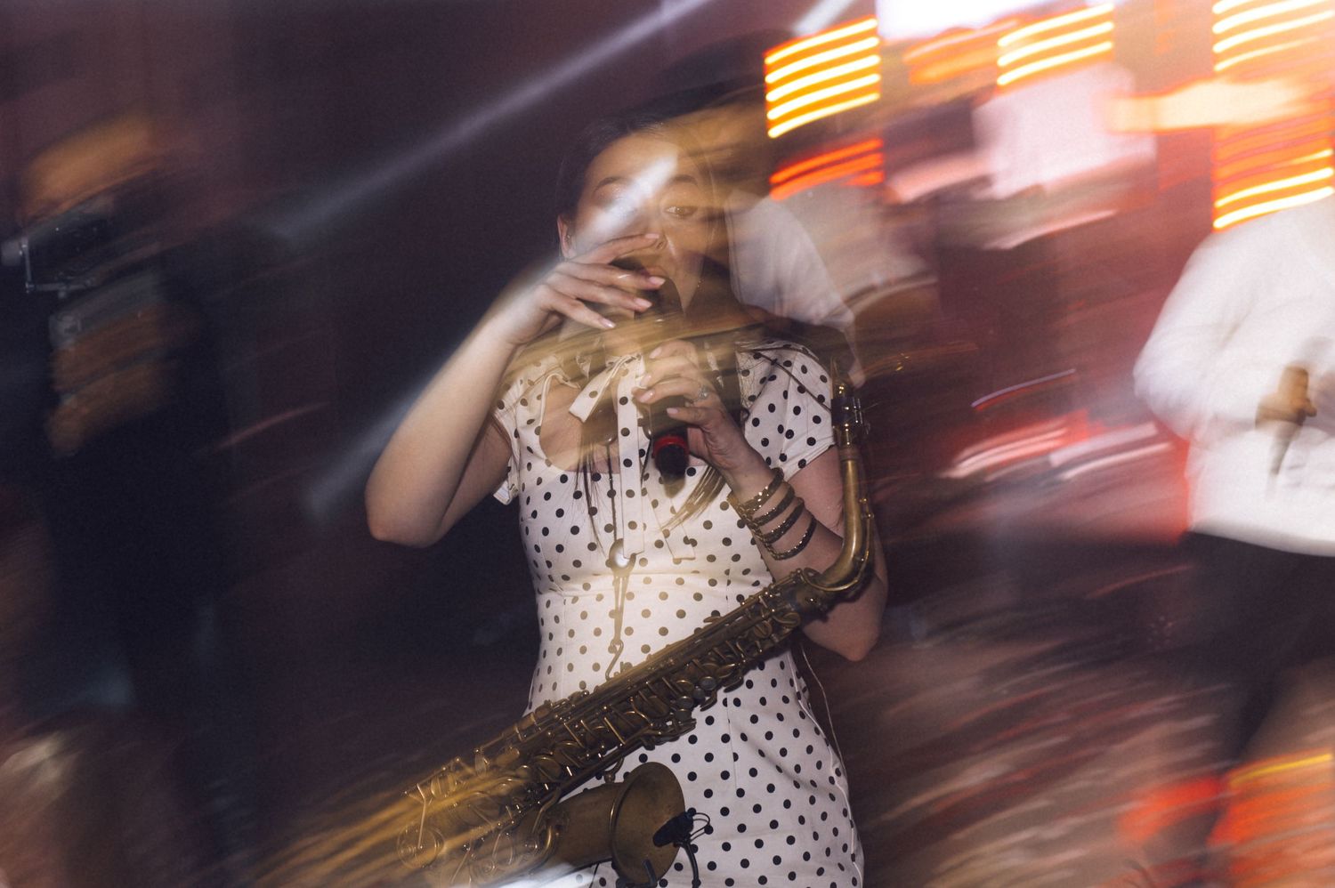 Blurred motion shot of a woman in a polka dot dress holding a drink at a vibrant nightclub event.