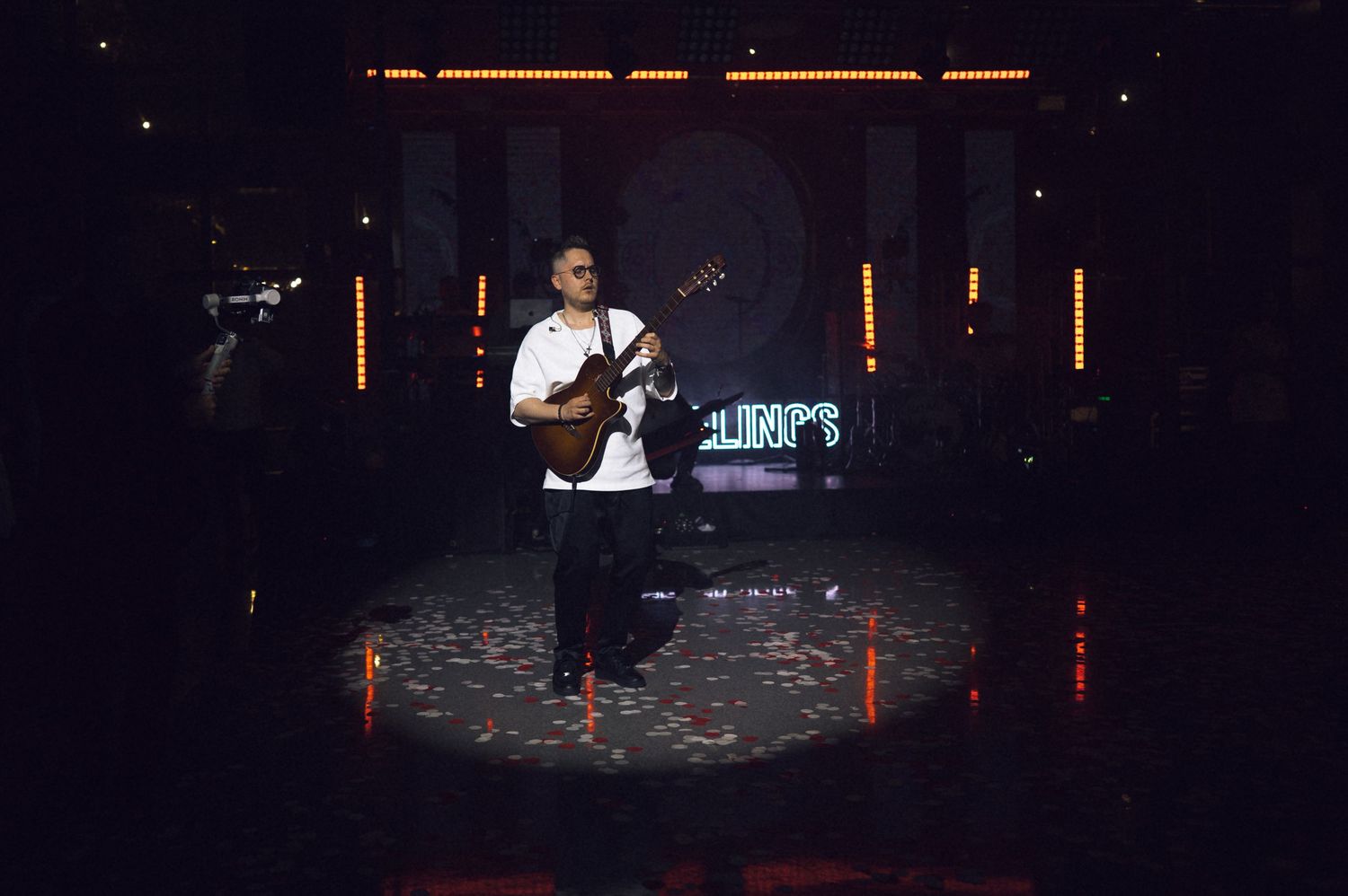 Man playing ukulele on a spotlight stage with orange LED lights and a dark background.