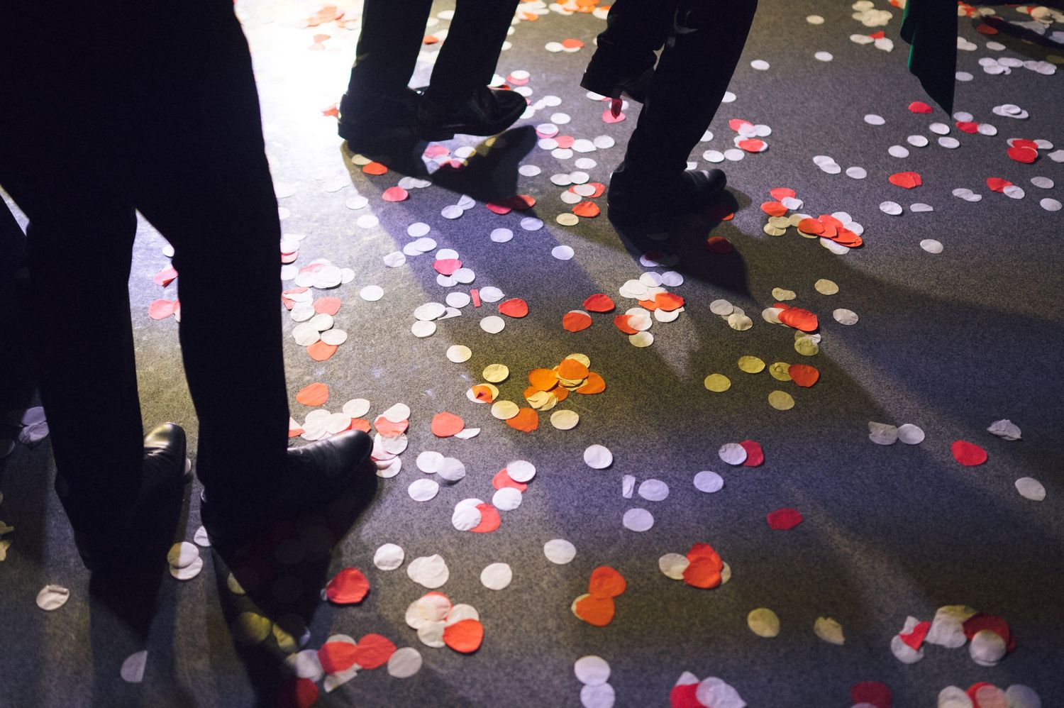 Colorful confetti scattered on dark floor with people standing around at a festive celebration event.
