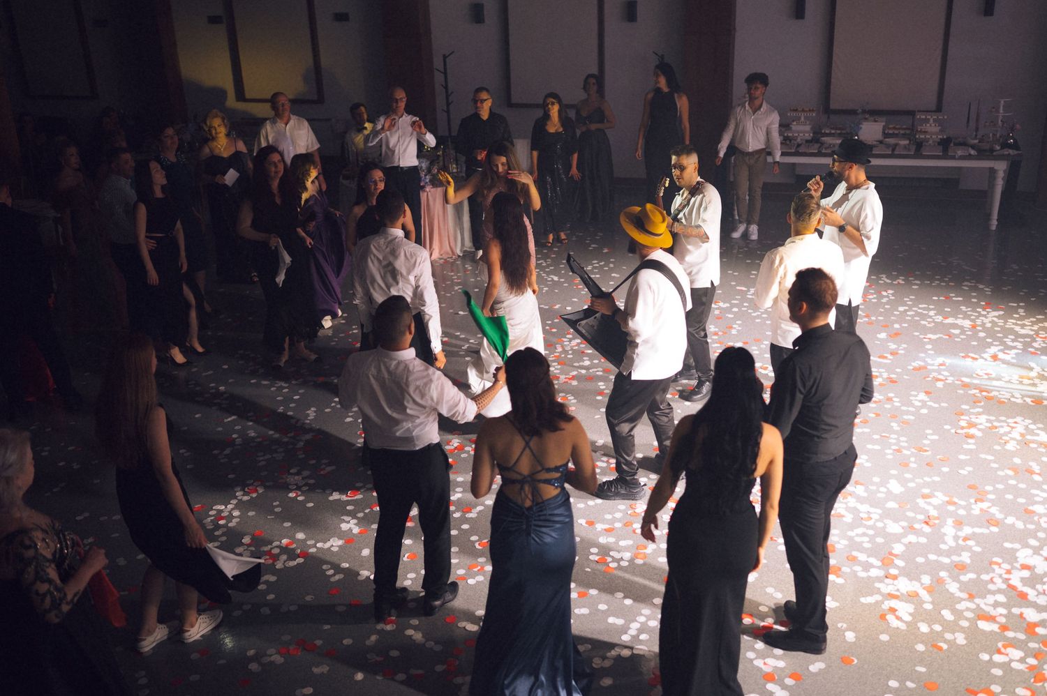 Elegant party guests dancing on a confetti-covered floor at a formal event with live musicians performing.
