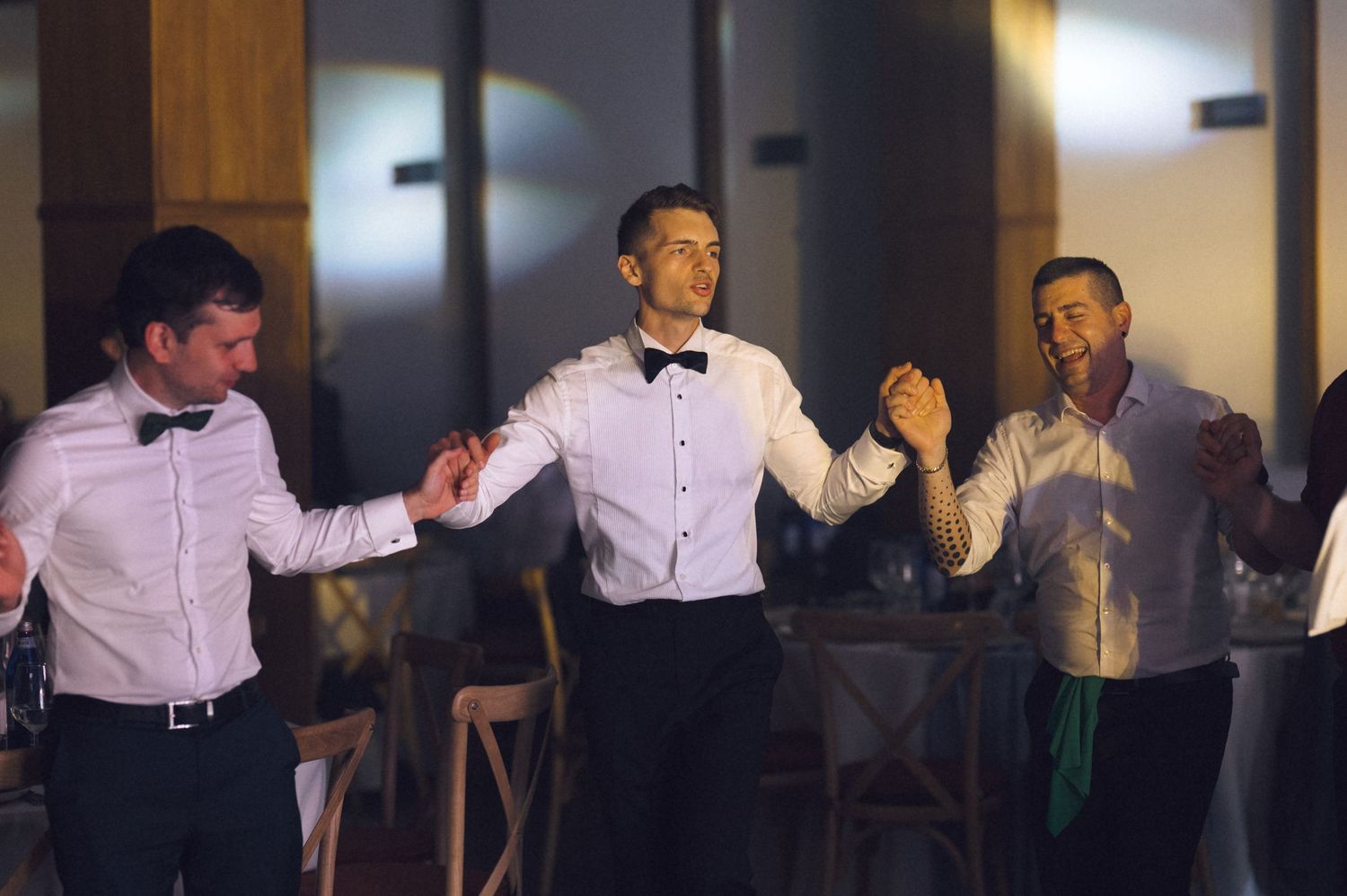 Three men in white dress shirts dancing together at a formal wedding reception celebration.