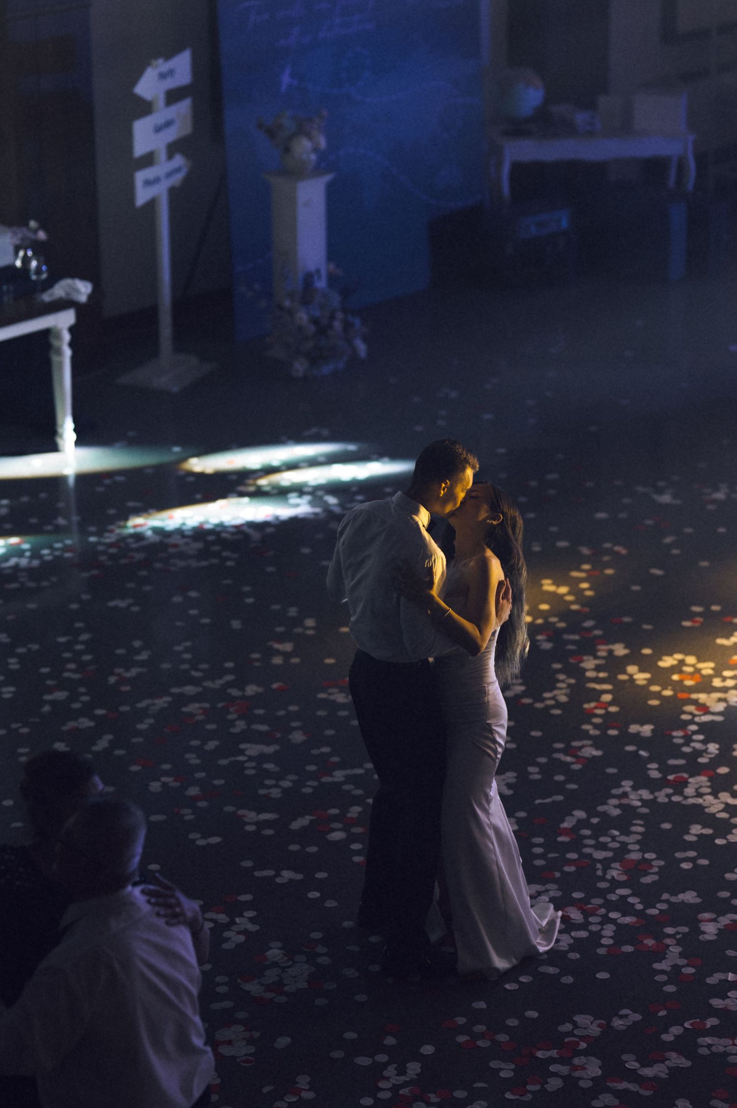 Couple sharing first dance at wedding reception on flower petal decorated floor under romantic spotlight.