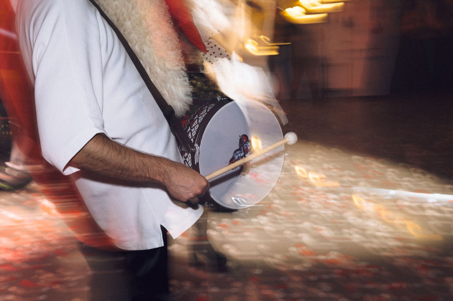 A musician plays a traditional drum while walking, captured with motion blur in a vibrant outdoor setting.