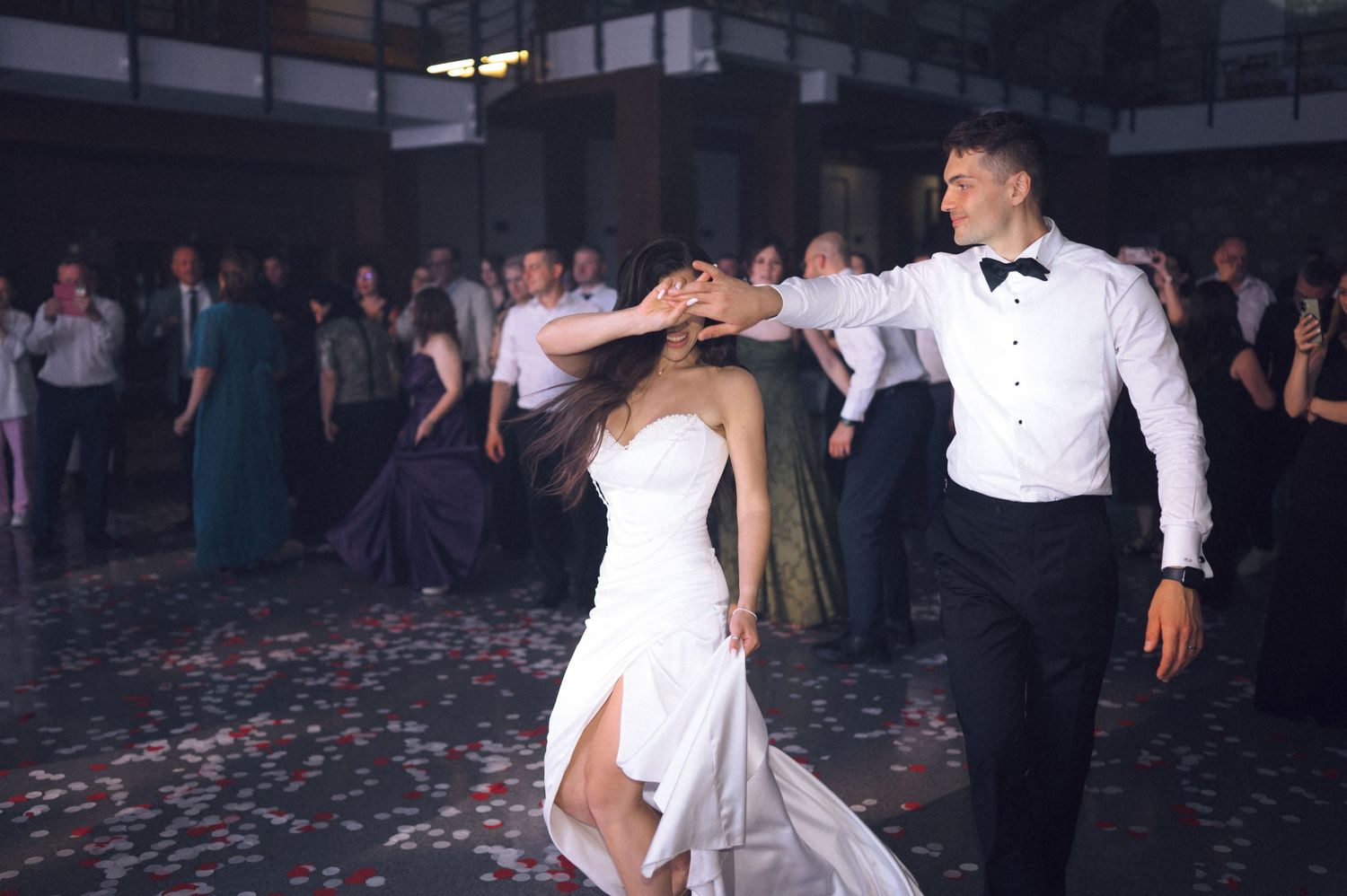 Bride and groom share first dance at wedding reception, guests watching in background.
