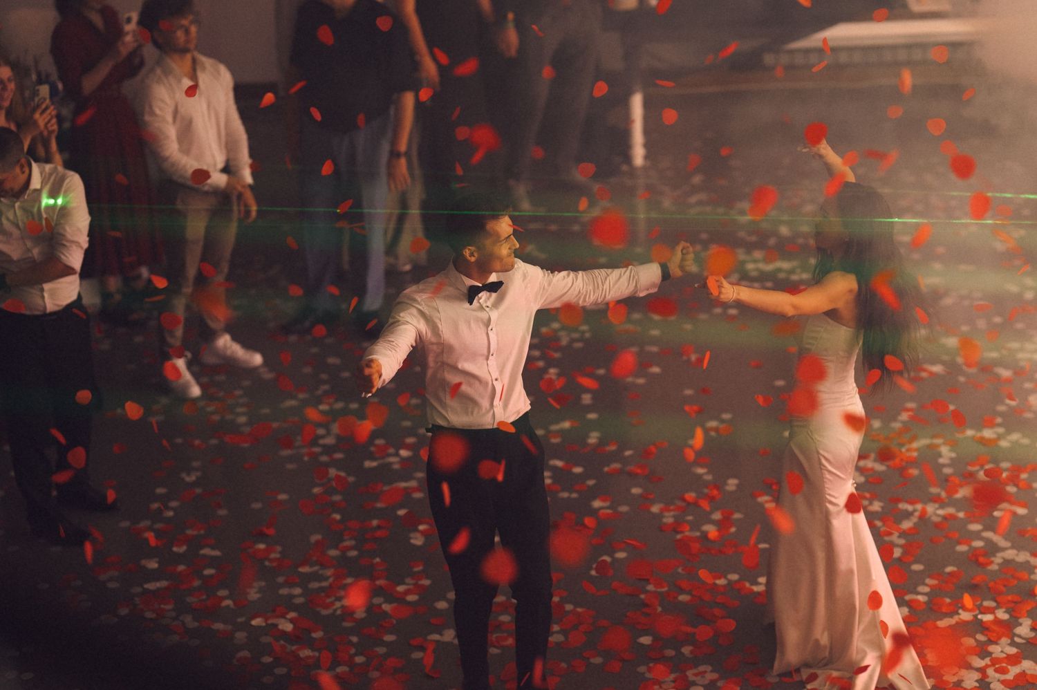 Couple dancing romantically surrounded by falling red rose petals at an elegant wedding reception.