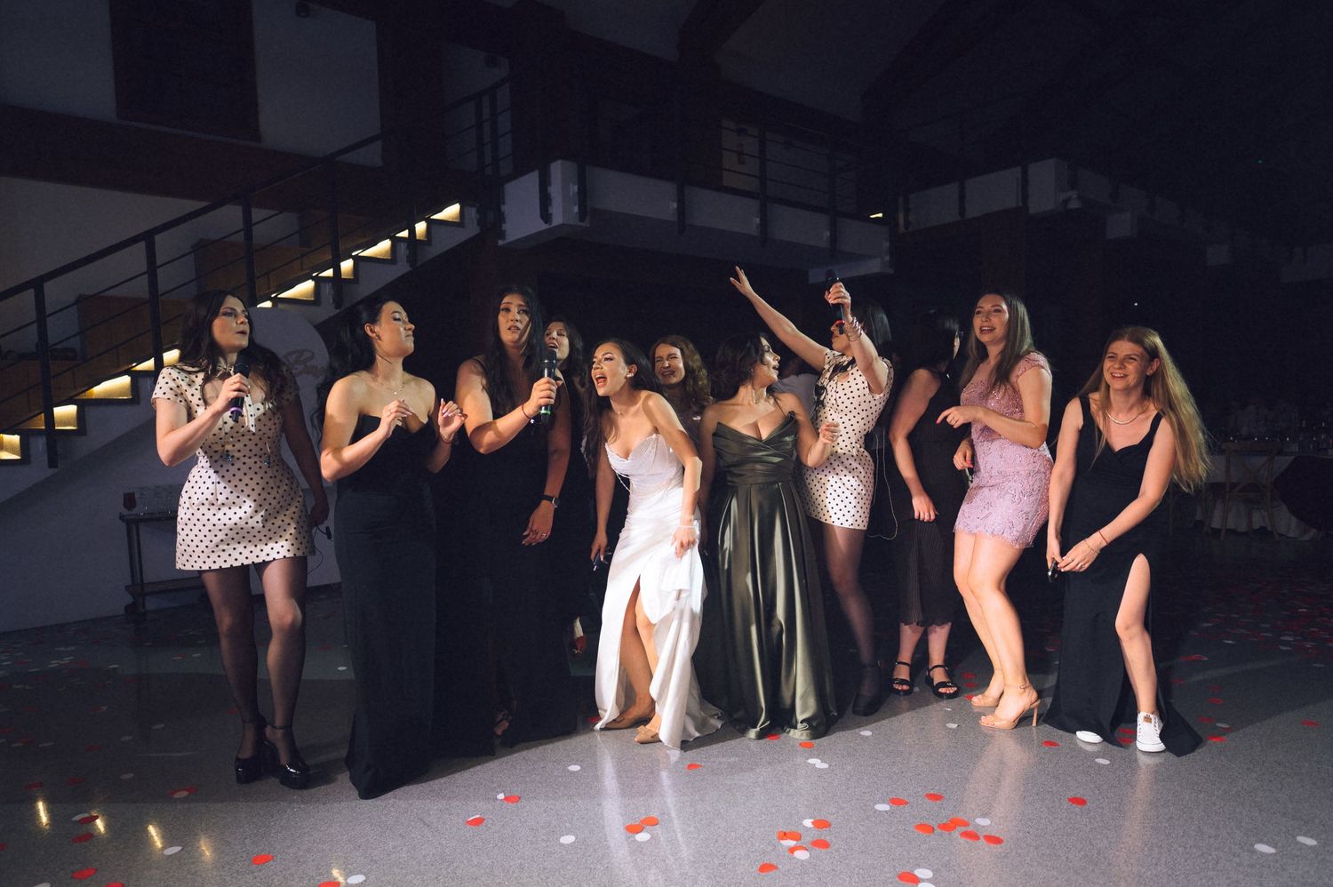Group of women in elegant dresses dancing and celebrating on a dance floor with rose petals.