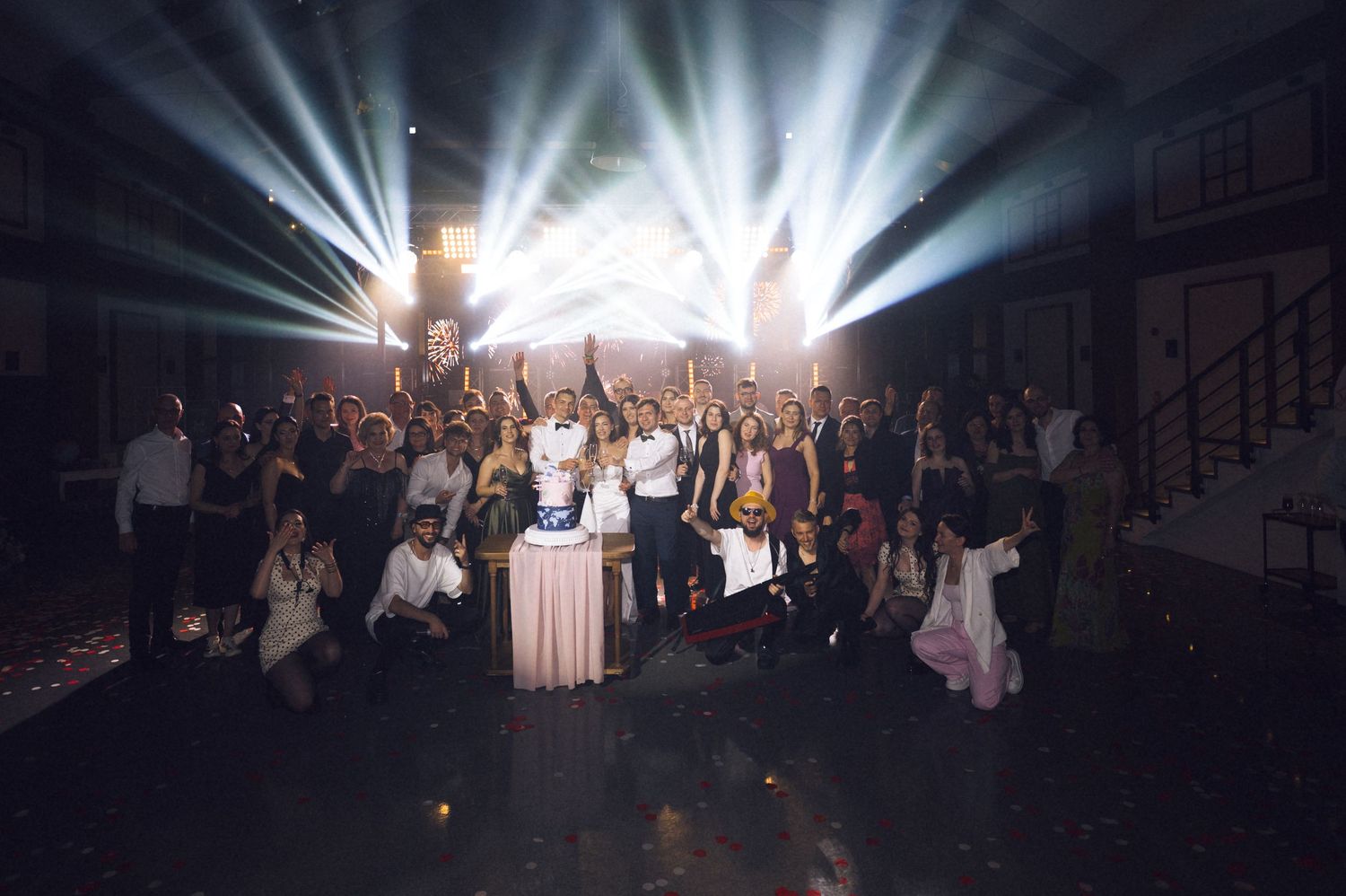Large group photo at elegant event venue with dramatic stage lighting and beams in background.