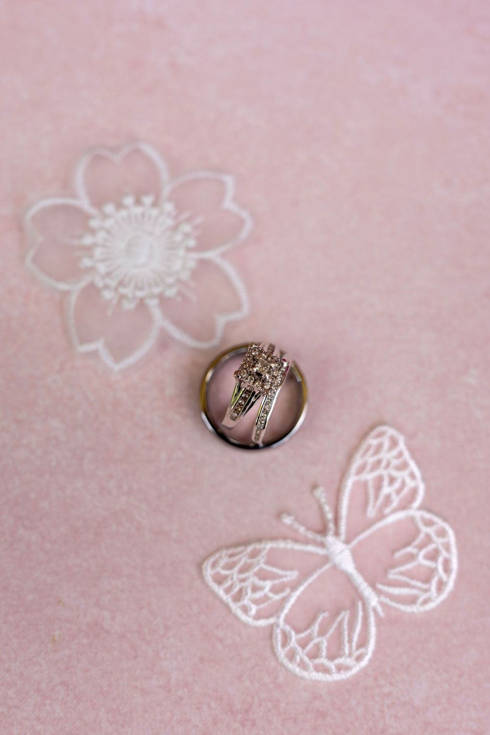 Elegant round brooch with cross design on pink embroidered fabric with delicate flower and butterfly lace details.