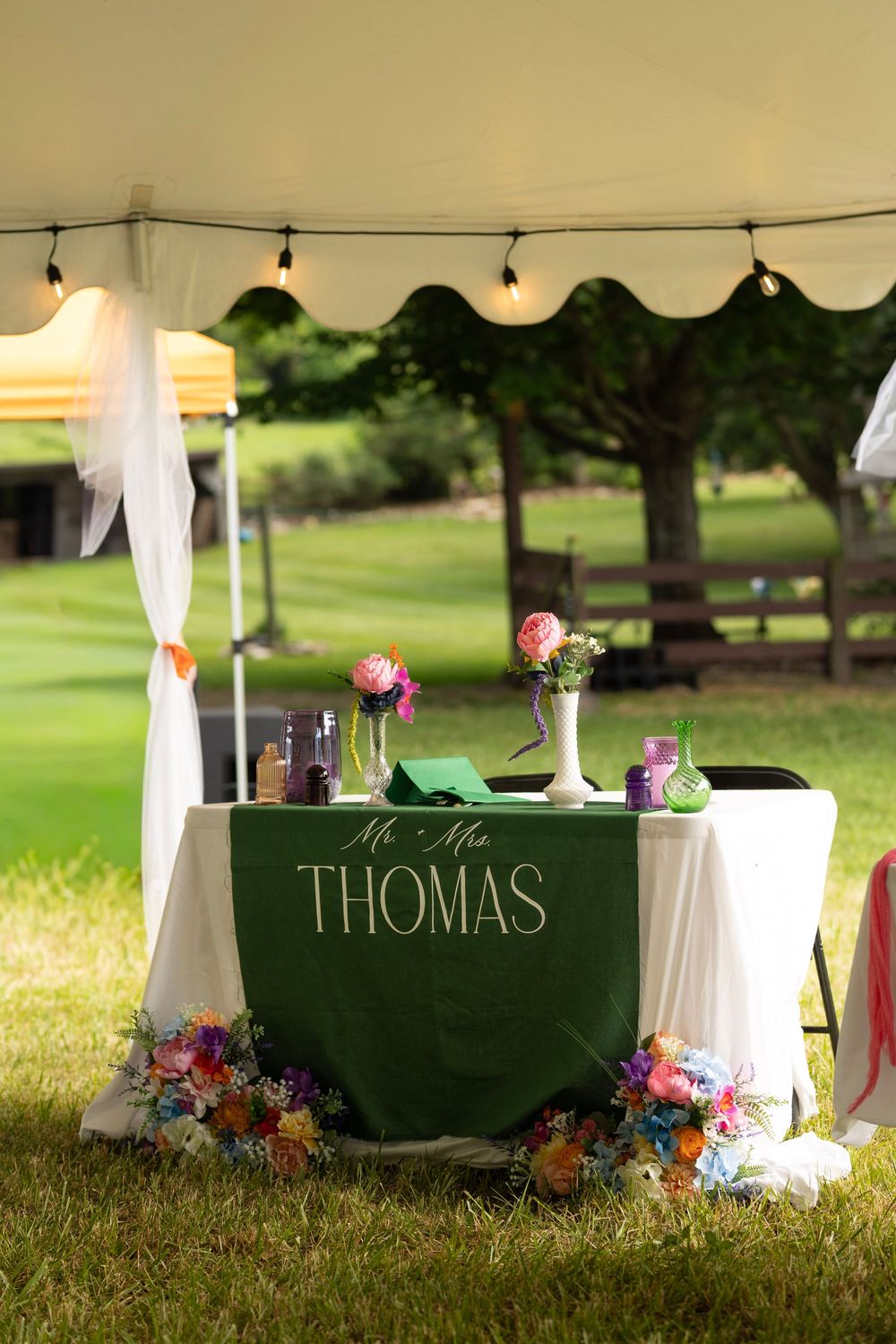 Green Mr. and Mrs. Thomas sweetheart table decorated with colorful floral arrangements under a white reception tent.