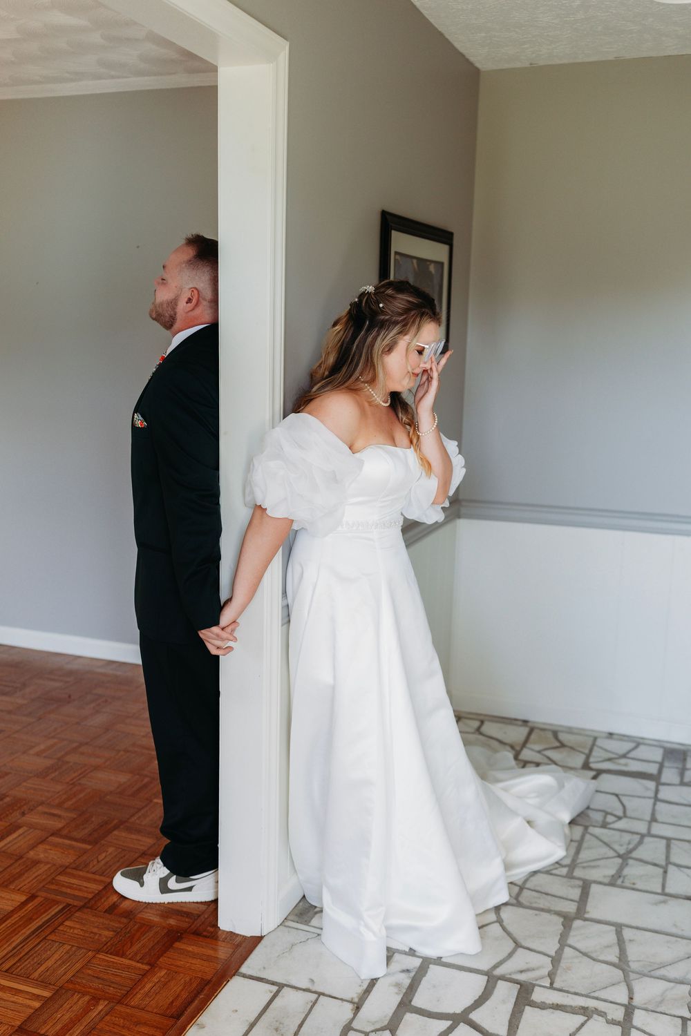 Bride and groom sharing emotional first look moment separated by doorway before ceremony.