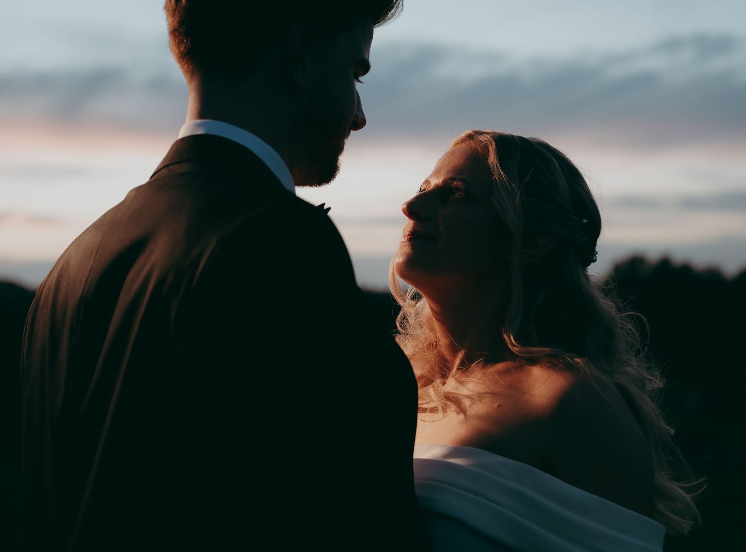 Silhouette of bride and groom sharing romantic moment at twilight with colorful sky backdrop at wedding.