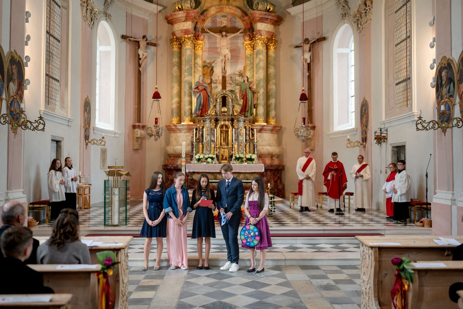 Firmlinge stehen mit dem Priester vor dem Altar in einer Barockkirche