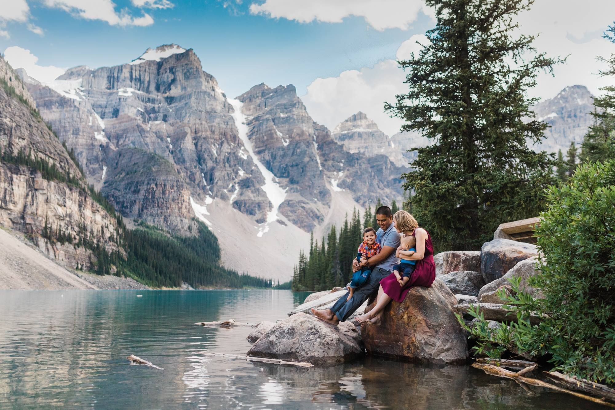 Family sitting on a rock at Moraine Lake with turquoise water and Rocky Mountain peaks in Banff, Canada.