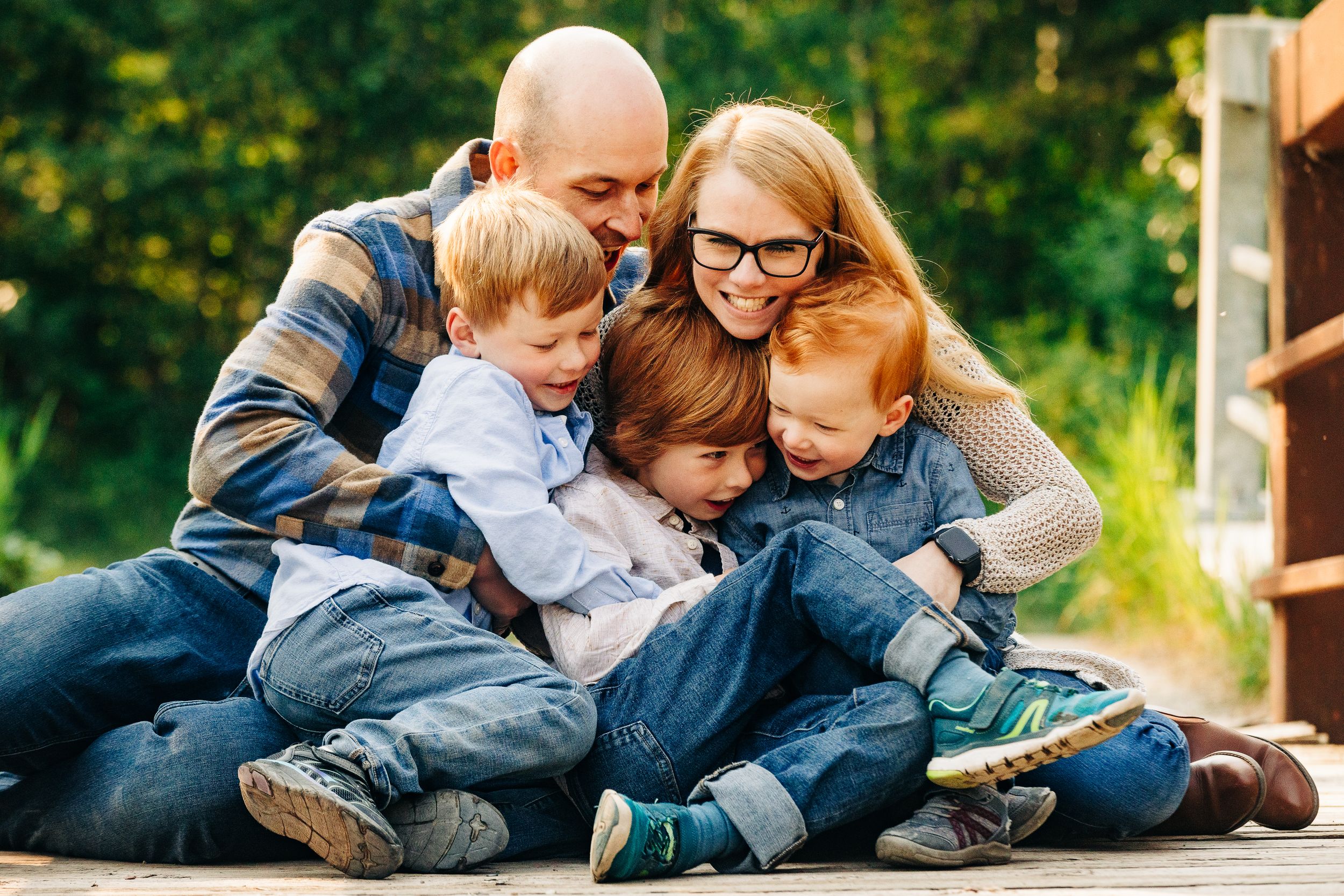Happy family of five sharing a warm hug outdoors, with two parents embracing three red-haired boys on a wooden deck.