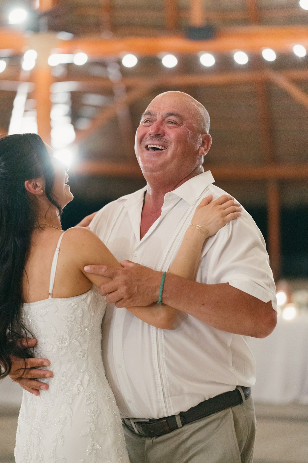 A joyful father-daughter dance at a wedding reception, with string lights glowing in the background.