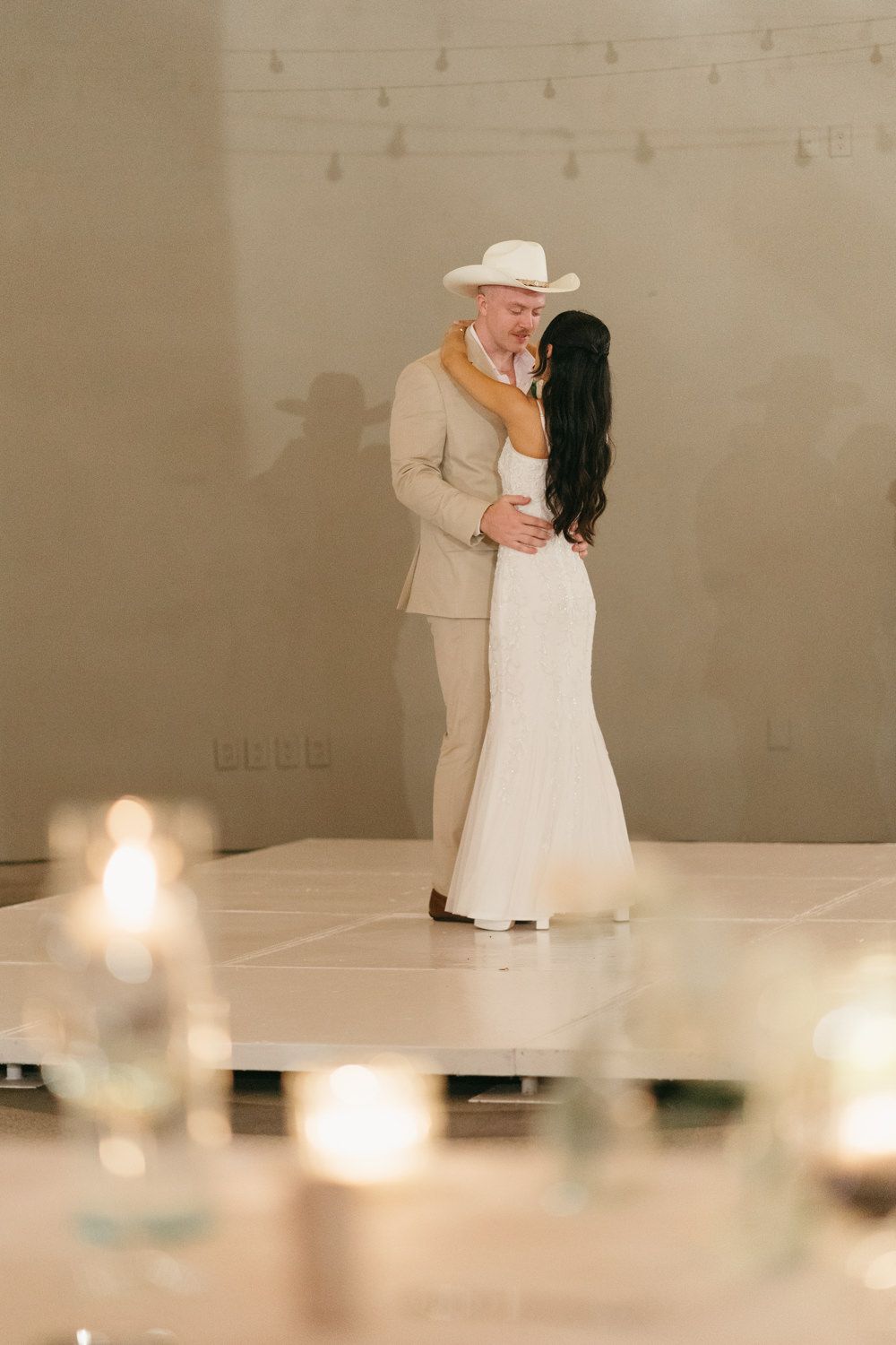 Bride and groom share their first dance on a white dance floor with candles glowing in the foreground.