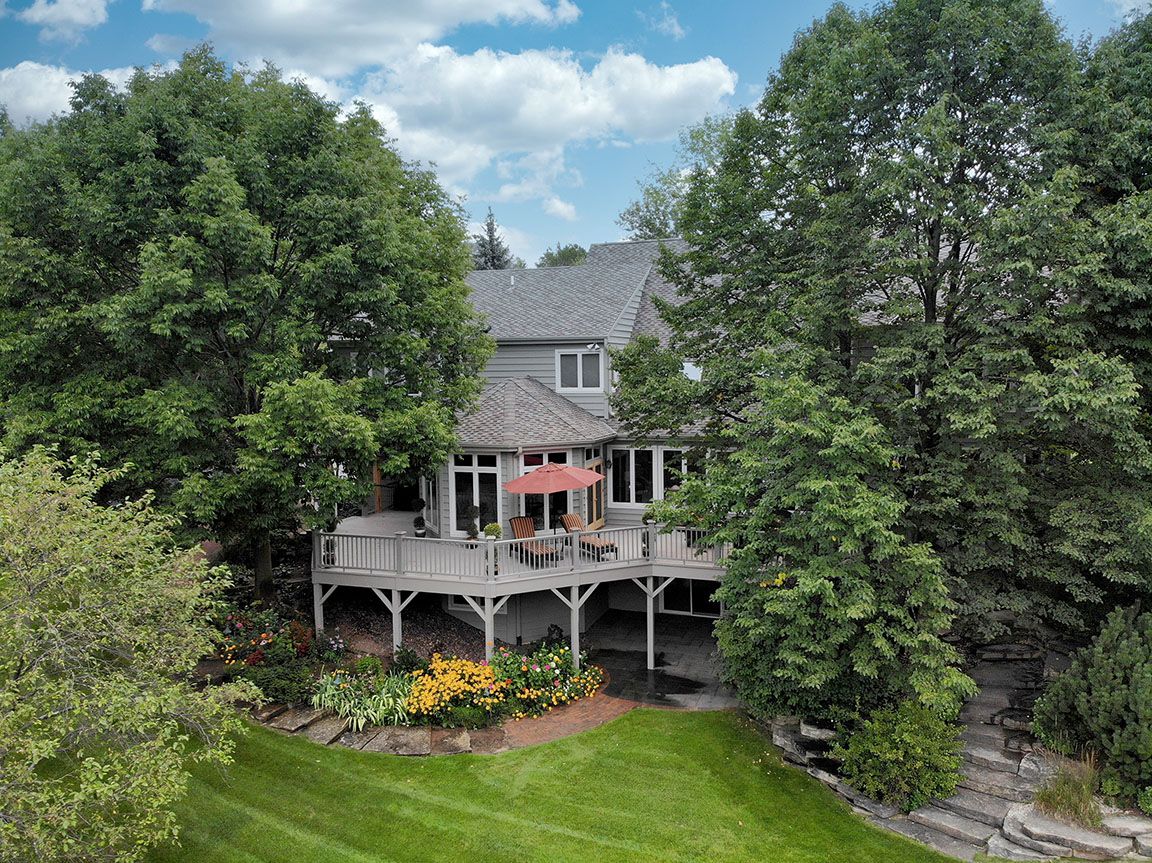 Aerial drone photo of a home with covered deck surrounded by mature trees, Milwaukee area