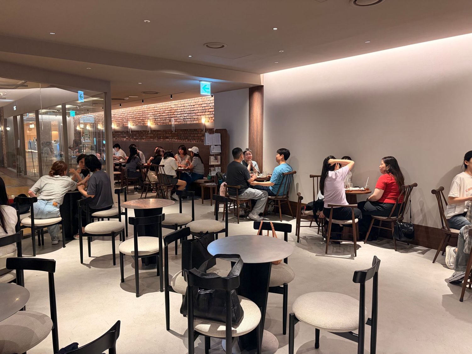 Modern cafe interior with patrons seated at round tables in a bright, minimalist space with warm accent lighting.