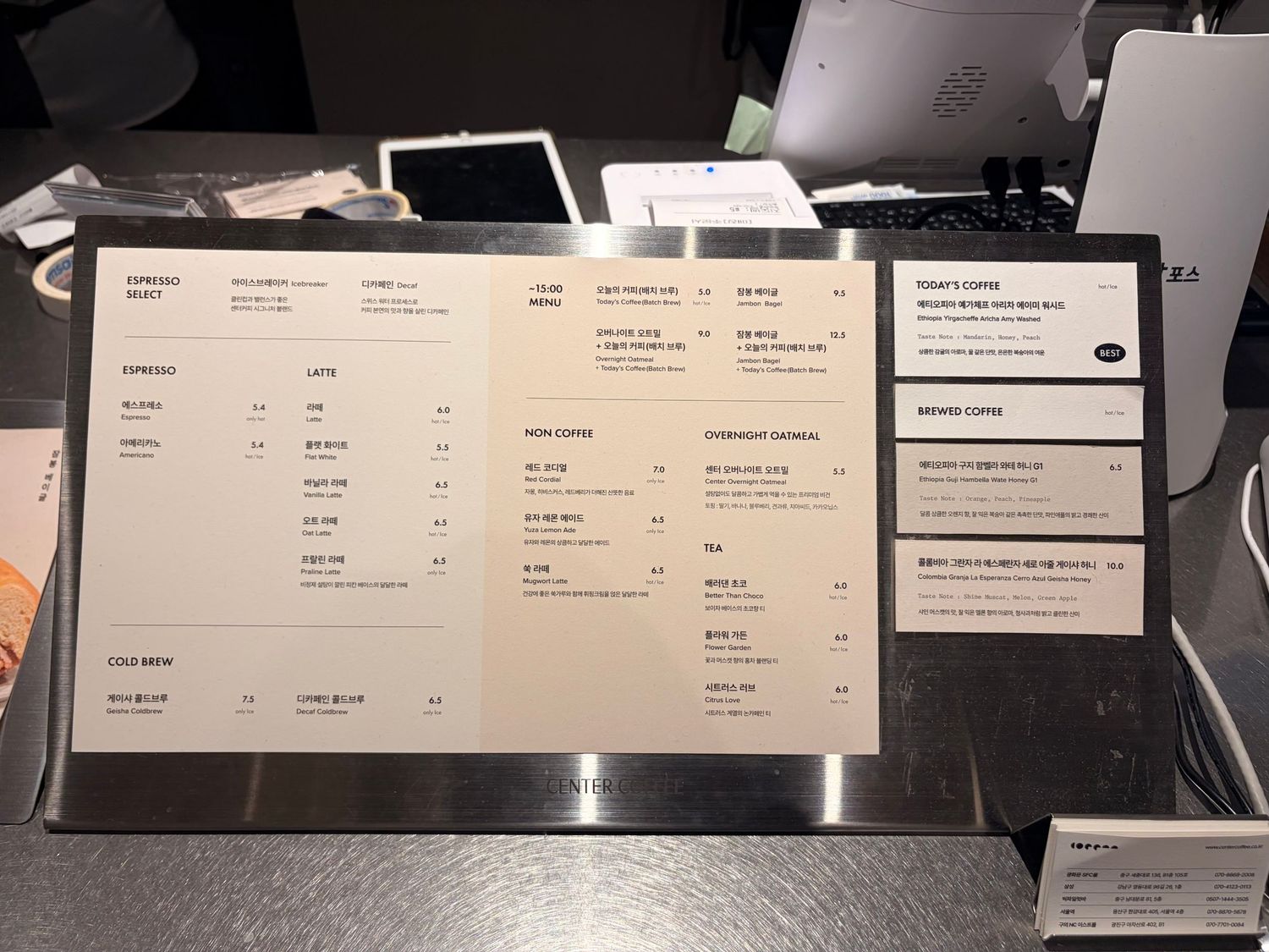 A coffee shop menu board displayed at a counter, featuring various drinks and options in a modern minimalist design.