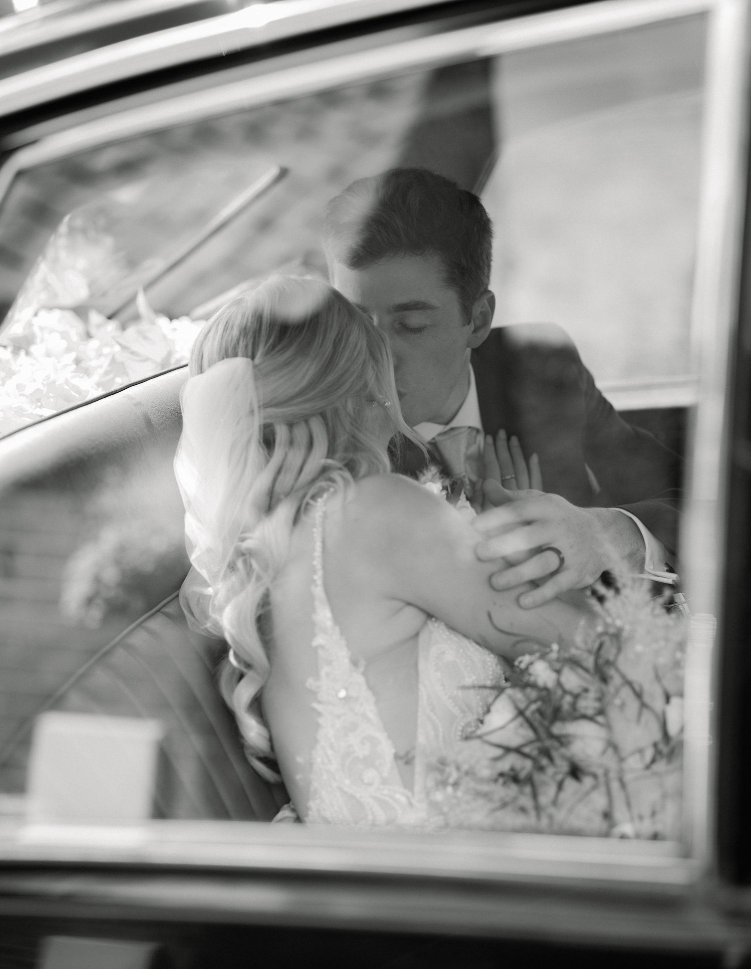 Smiling newlyweds walk hand-in-hand from a stone church arch, bride holding white bouquet, groom in dark suit, confetti falling.