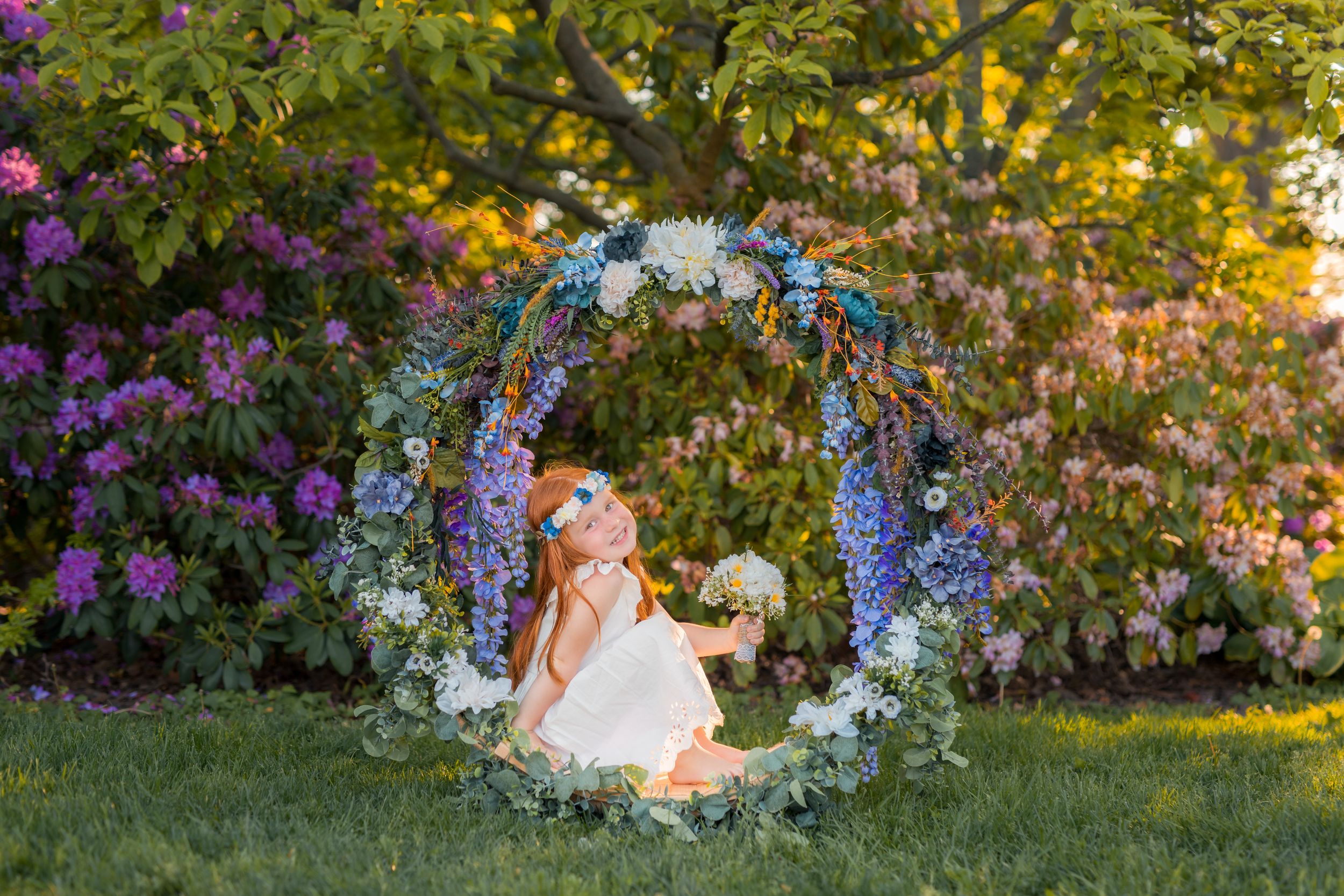 Red-haired girl smiling beneath a handcrafted floral display at Kings Navy Yard Park.