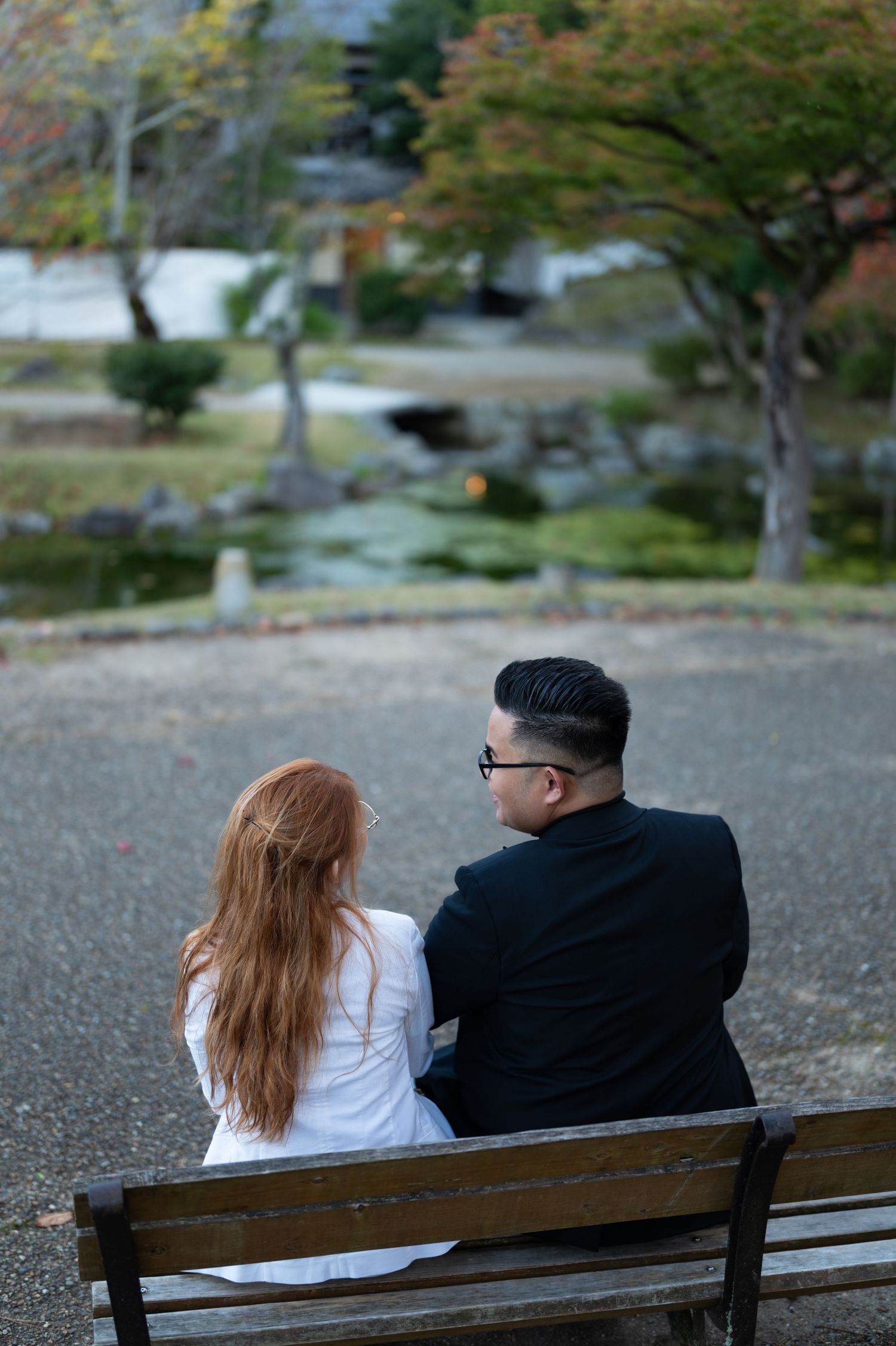 Couple sitting together on a bench in a serene Japanese garden during autumn.