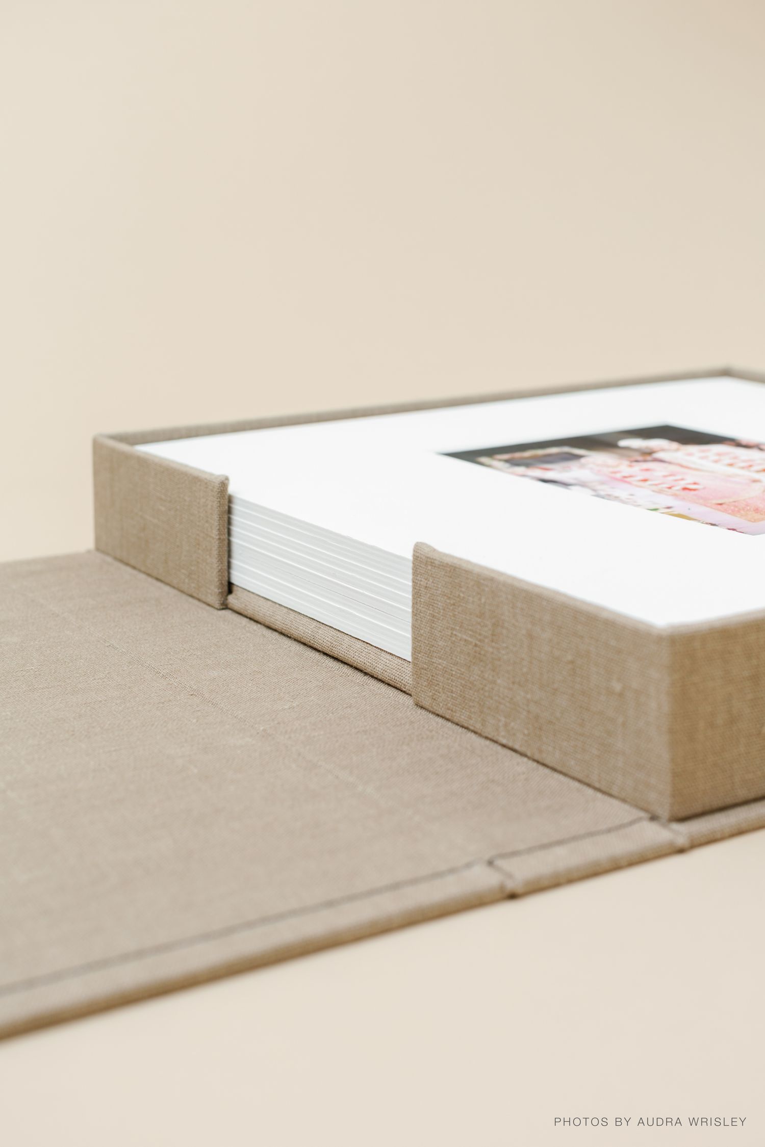 Elegant linen photo box with matted prints, open lid displaying stacked photographs on a neutral background.
