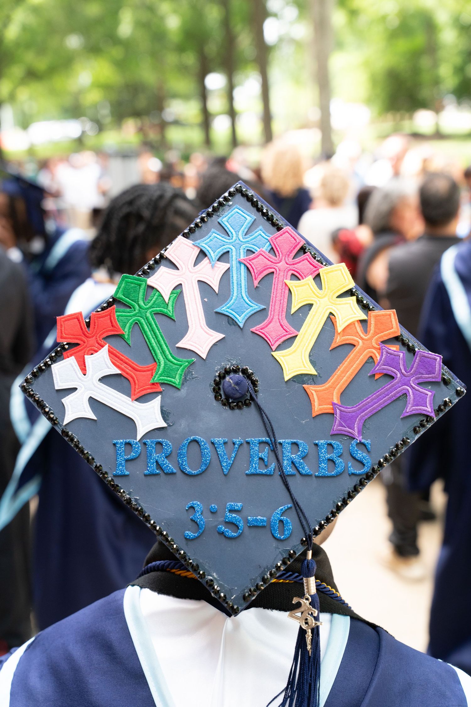Decorated graduation cap with colorful crosses and Proverbs 3:5-6 Bible verse at a graduation ceremony.