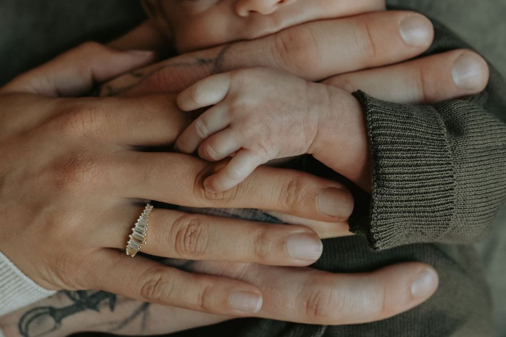 Close-up of newborn baby hand resting on parents hands, mother wearing diamond ring, family bonding moment.