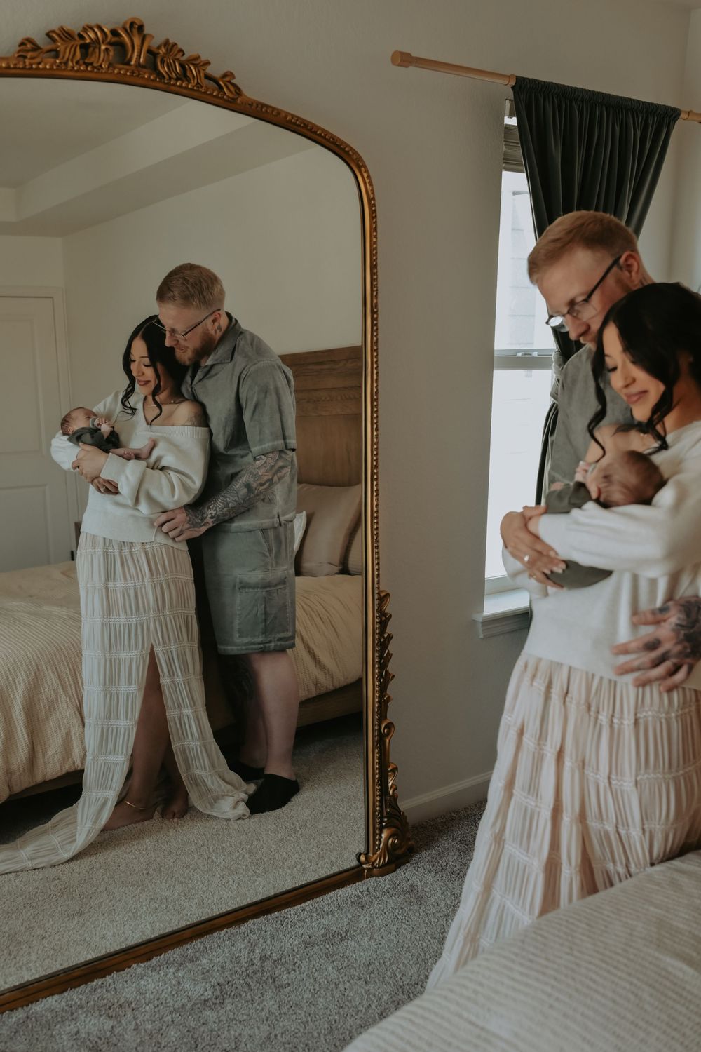 Couple holding newborn baby reflected in ornate gold mirror in bedroom, newborn lifestyle photography.