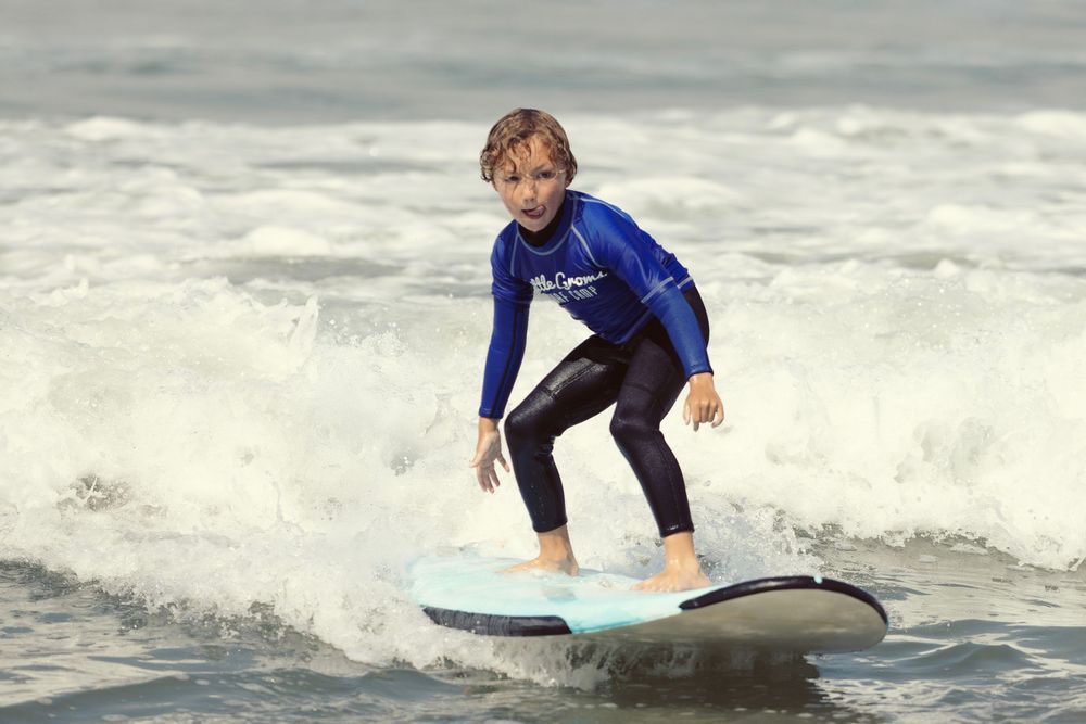 Young boy in blue wetsuit surfing a wave on a light blue surfboard in the ocean.