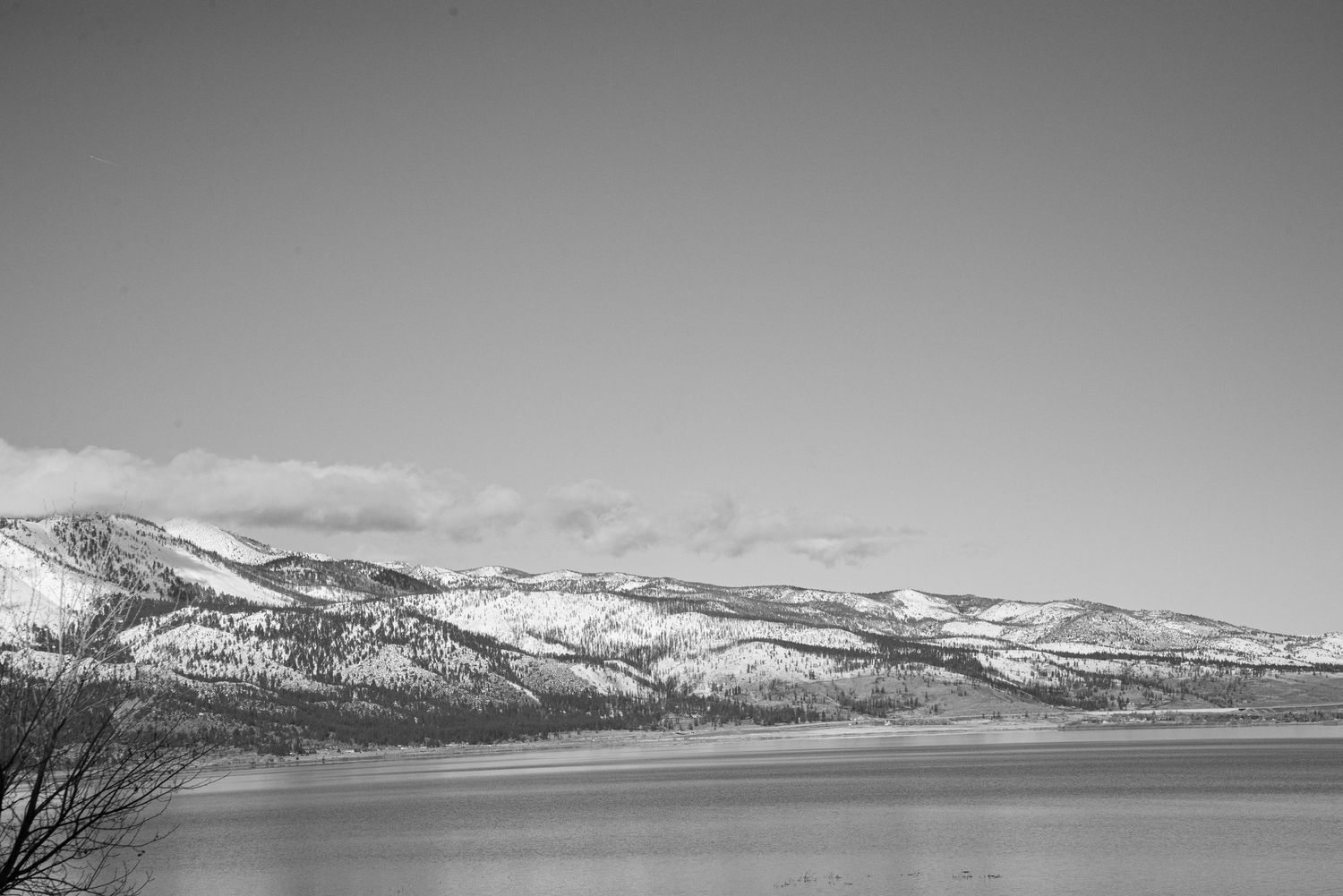 Black and white landscape of snow-capped mountains reflecting over a calm lake under clear sky.