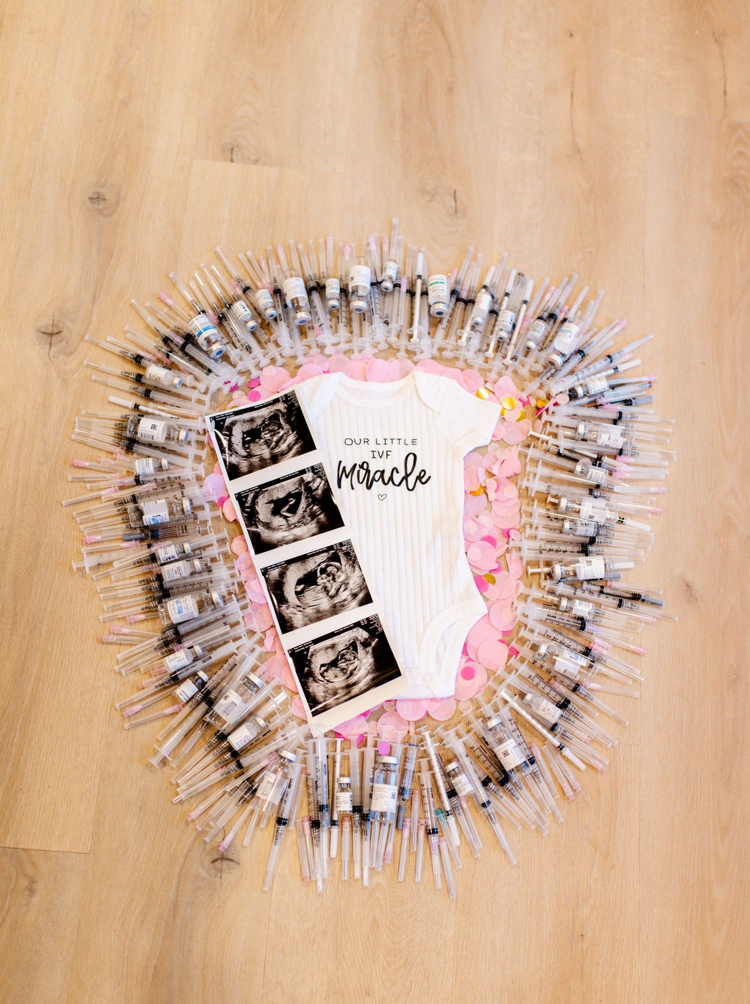 Heartfelt IVF pregnancy announcement flat lay featuring ultrasound photos and baby onesie captured by Maile Rupe Photography.
