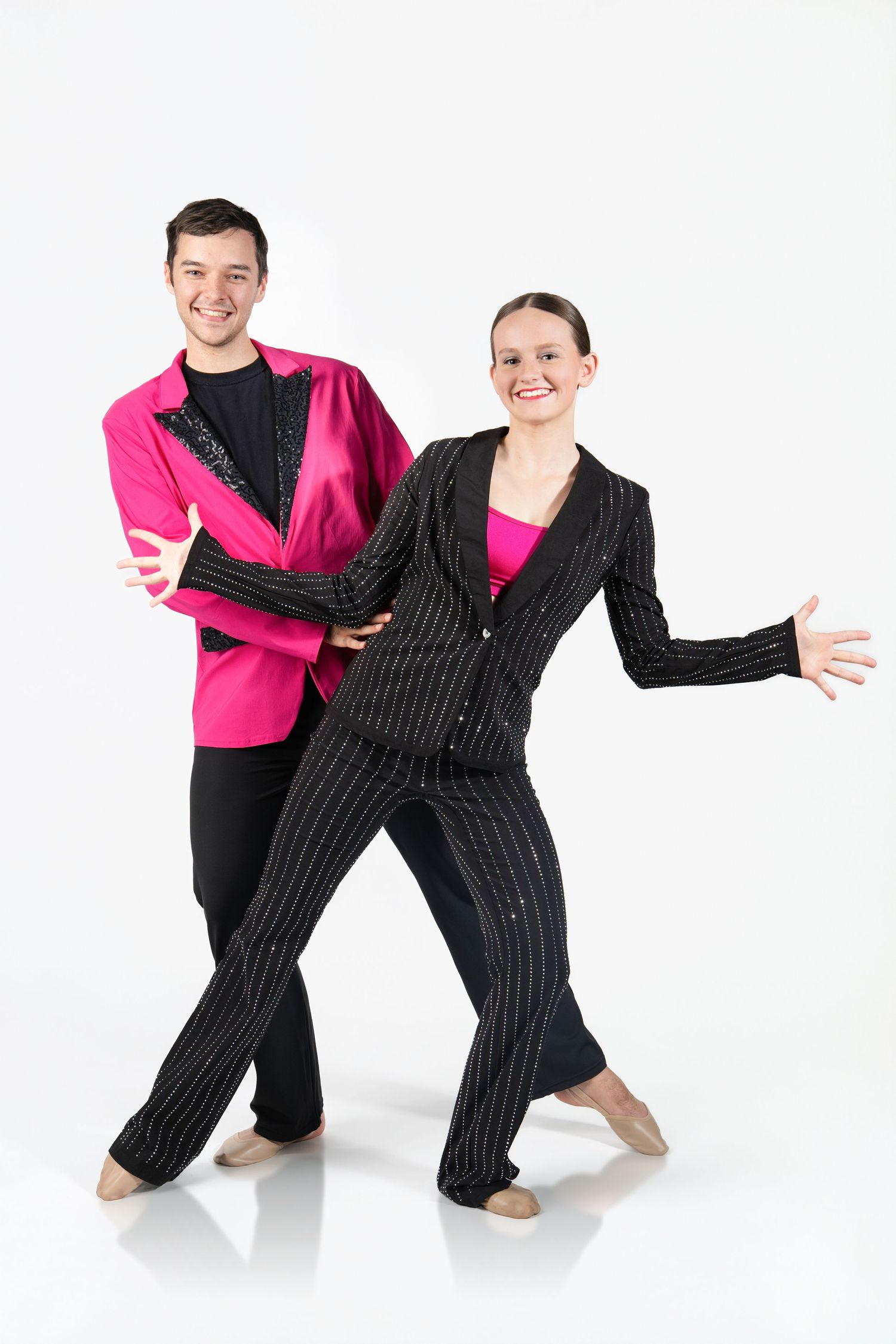 Man and woman in Jazz costumes striking a pose in studio with a white background. Both are wearing pink and black.
