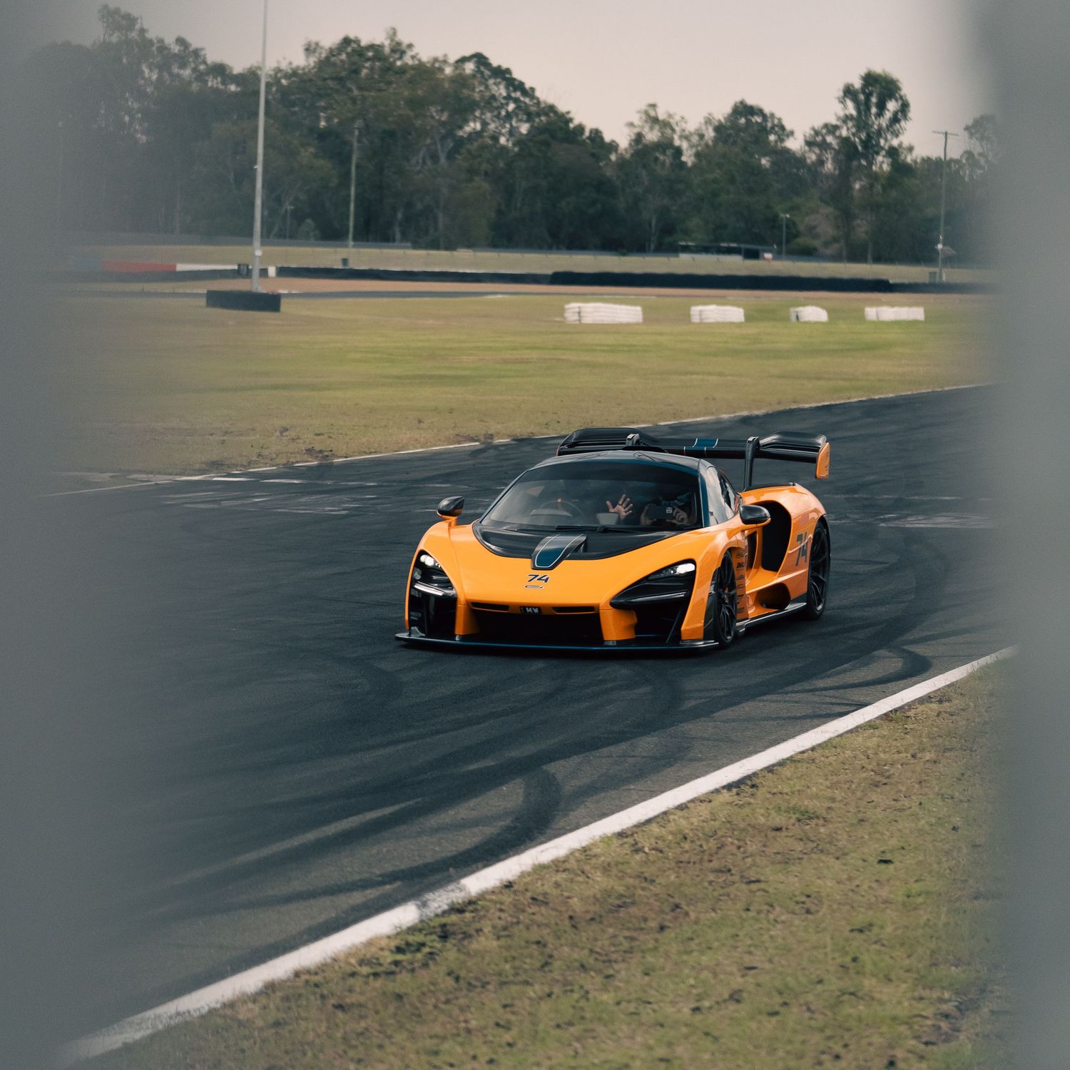 Orange McLaren Senna supercar cornering at speed on a racing circuit track.