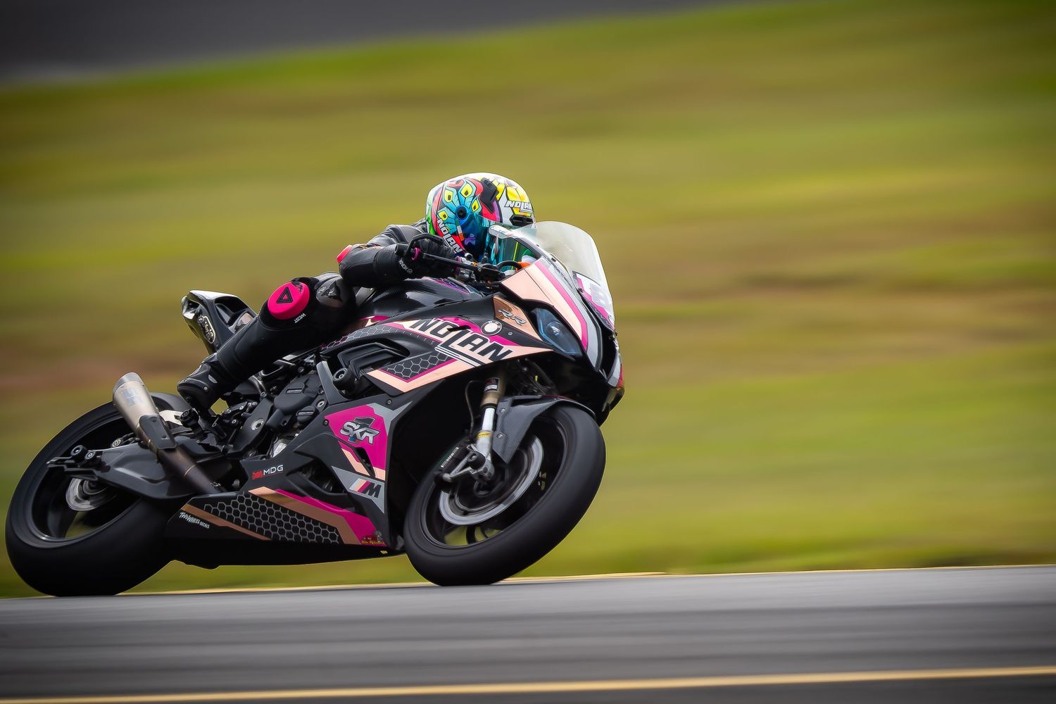 Rider on pink and black BMW superbike leaning into a corner on a wet racing circuit.