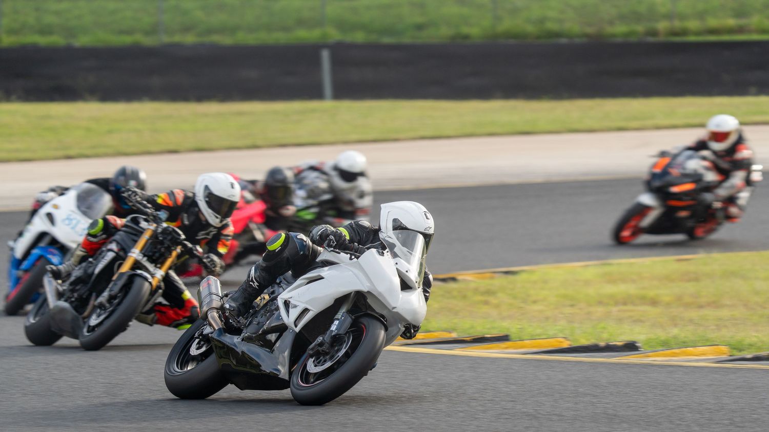 Group of sportbike racers led by white motorcycle navigating a corner on a racing circuit.