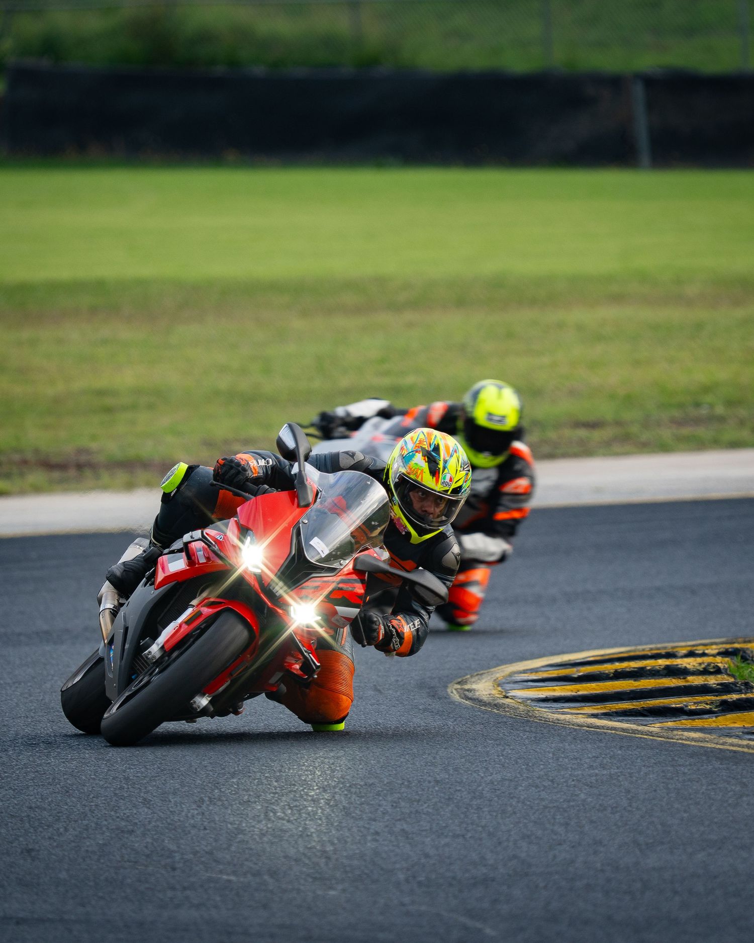 Two motorcycle racers on red Ducati and orange sportbike leaning through a tight track corner.