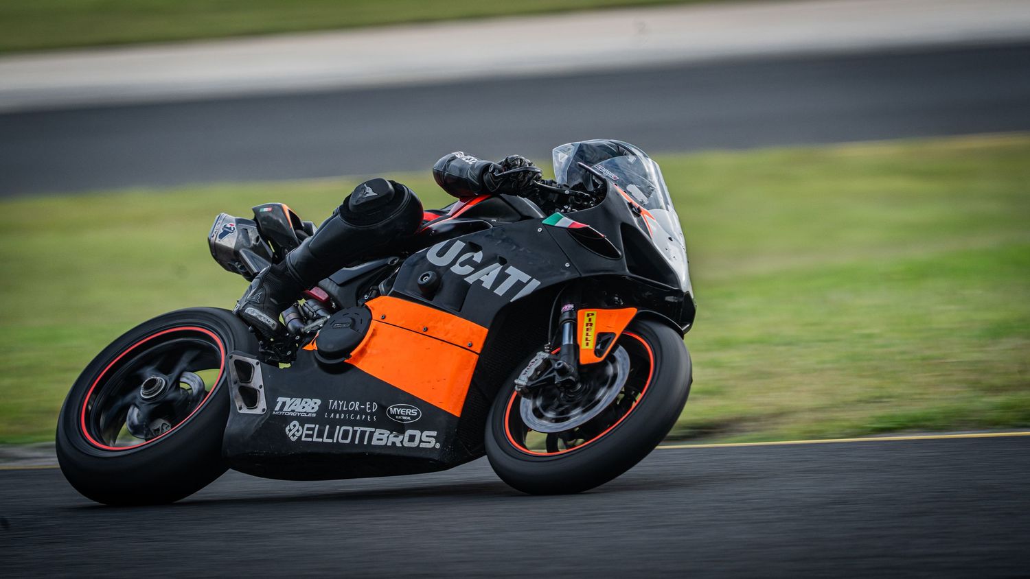 Black and orange Ducati superbike with Elliott Bikes livery cornering on a race track.