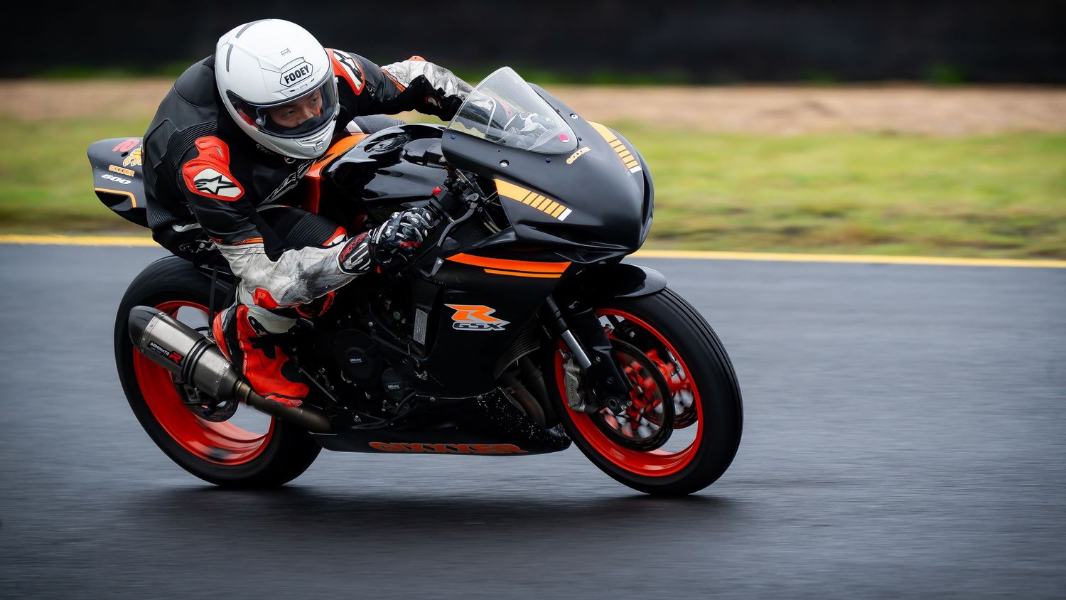 Rider on black and orange Suzuki GSX-R sportbike leaning through a wet racetrack corner.