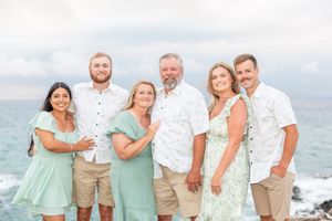 Family of six posing together on rocky ocean coastline in coordinating green outfits.