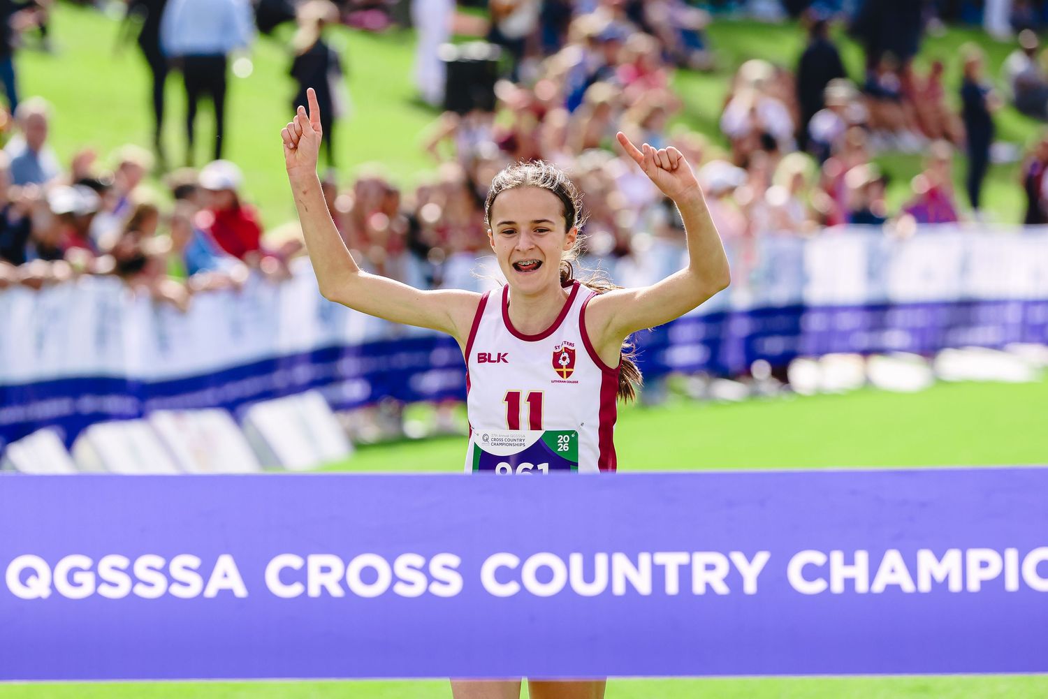 Female runner wearing blue uniform with number 76 crosses finish line at outdoor cross country race event.