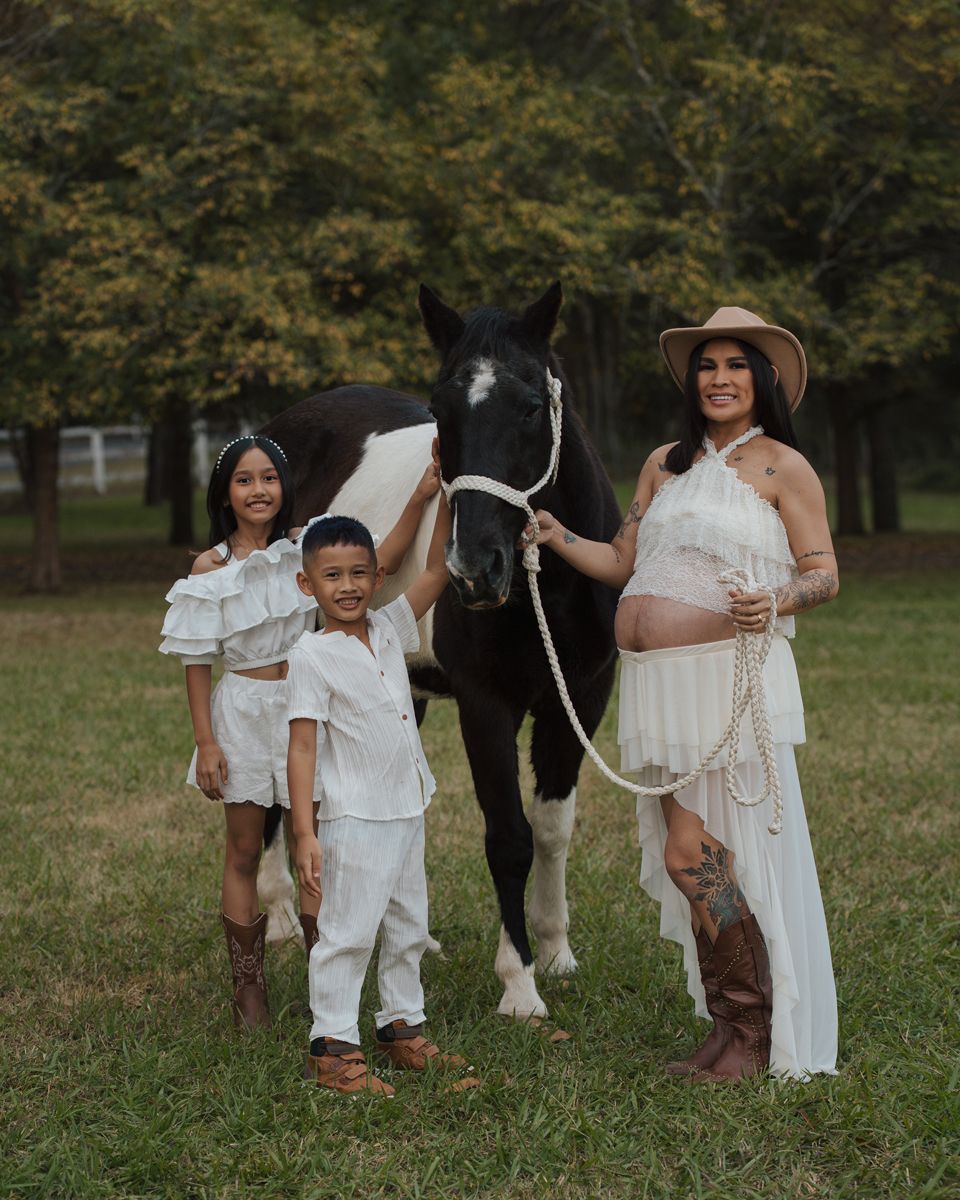 Pregnant woman in white dress with two children and a black horse outdoors during a maternity photo shoot in Sydney with a horse