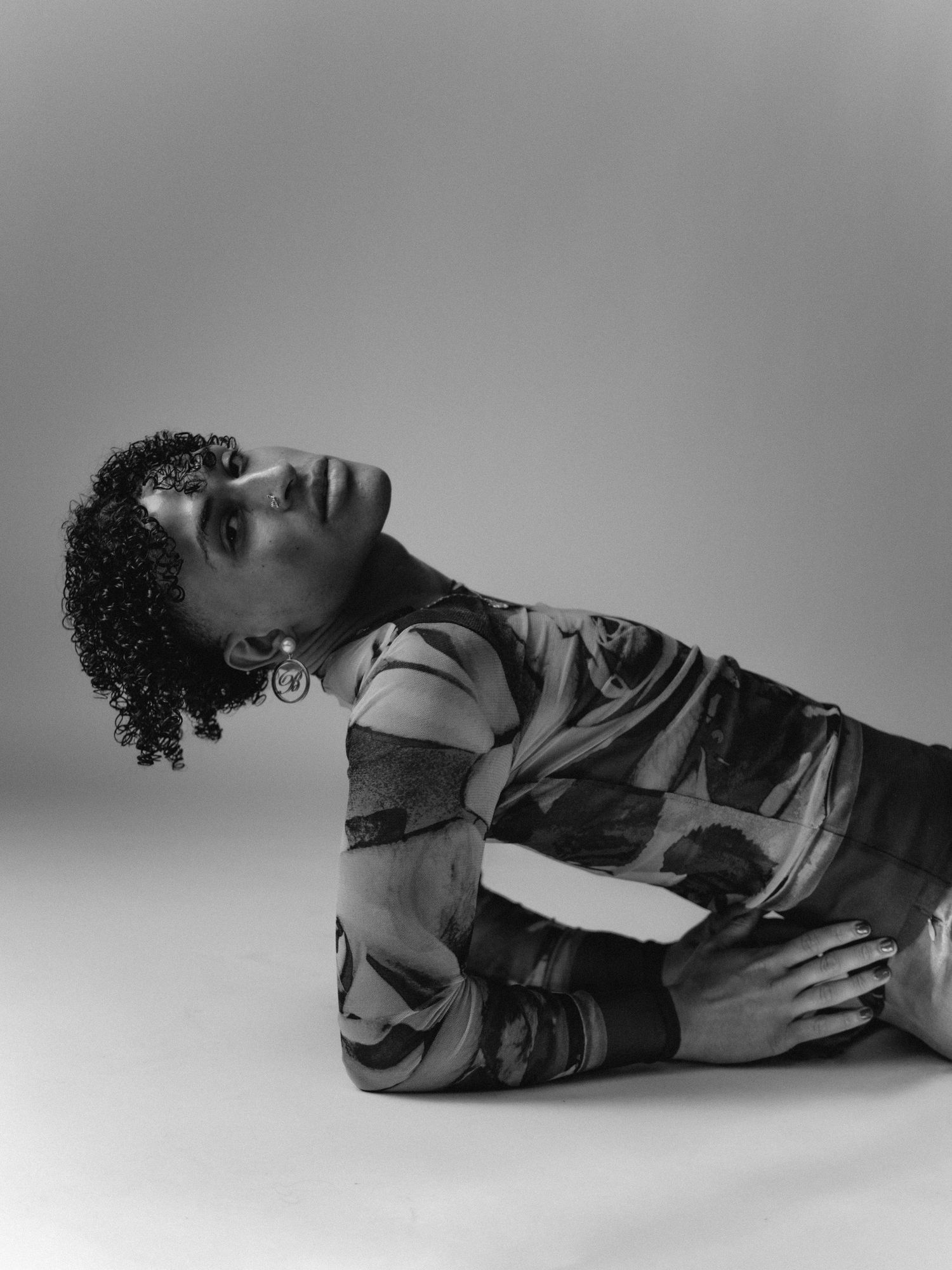 Black and white photo of a person in a patterned bodysuit posing gracefully on the floor with head tilted back.
