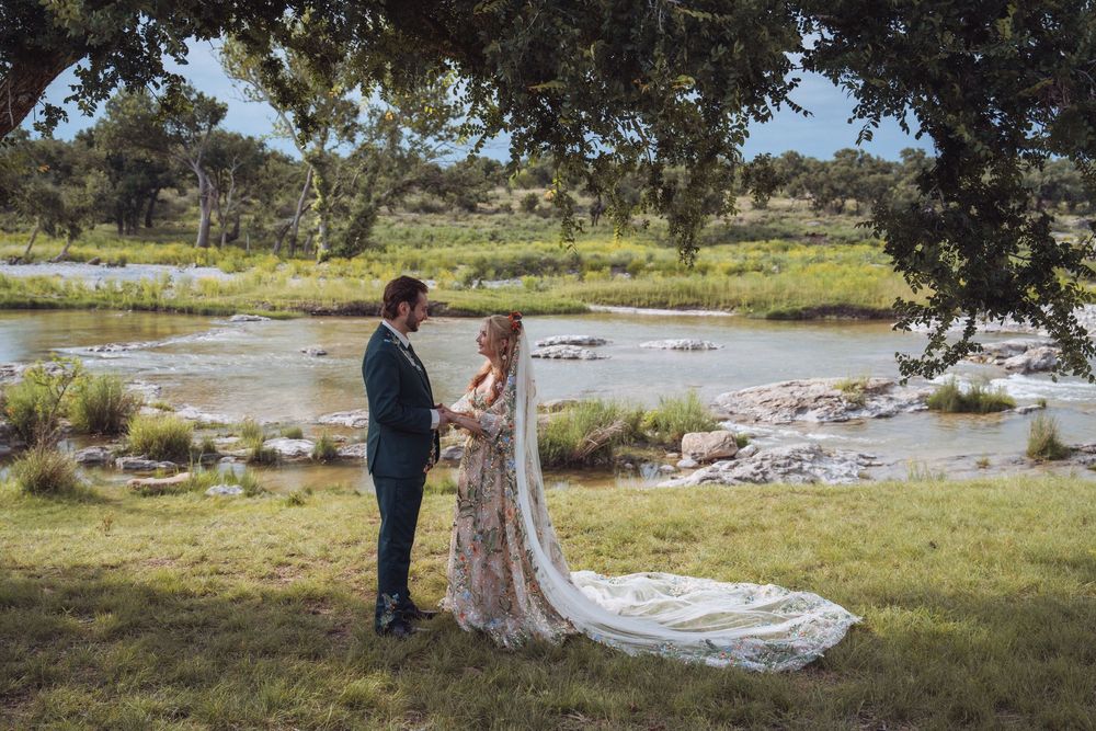 Bride and groom exchange vows by a scenic river surrounded by lush greenery on their outdoor wedding day.