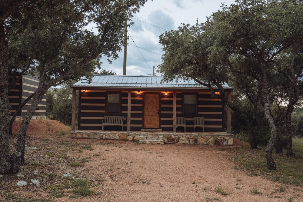 Rustic log cabin with warm lighting nestled among oak trees on a sandy Texas Hill Country property.