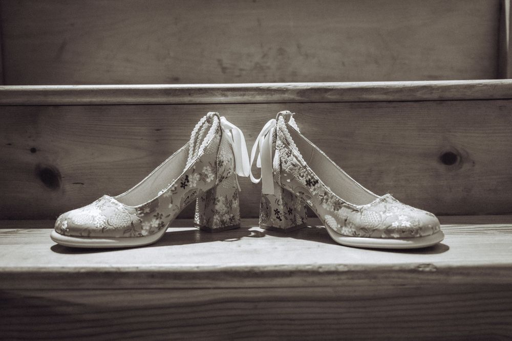 Elegant lace bridal heels displayed on a rustic wooden surface in a classic black and white wedding photo.