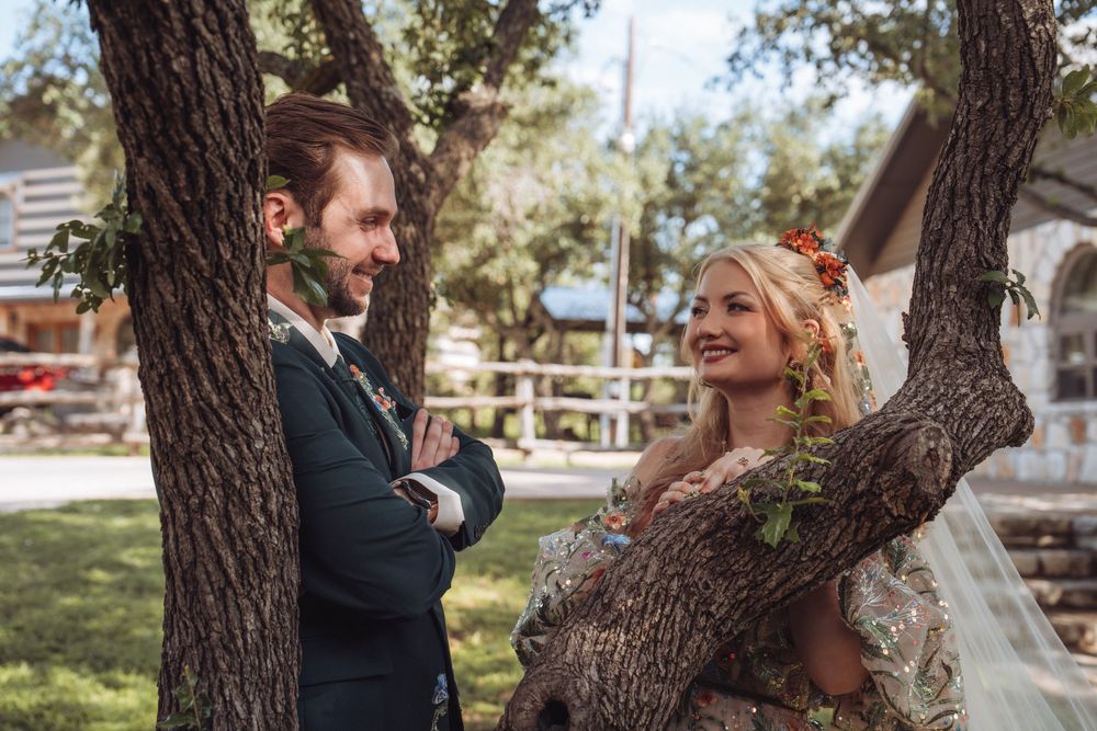Bride and groom share a joyful moment by a tree outdoors, bride wearing floral hair accessories and flowing veil.