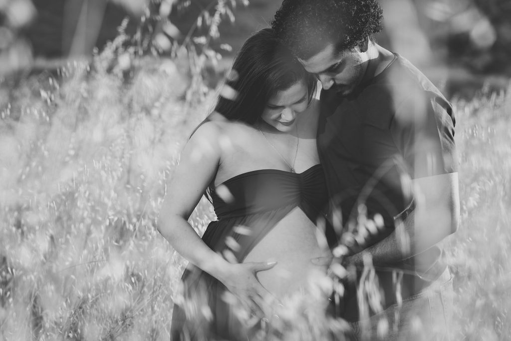 Black and white photo of a romantic couple embracing tenderly in a sunlit field of tall grass.